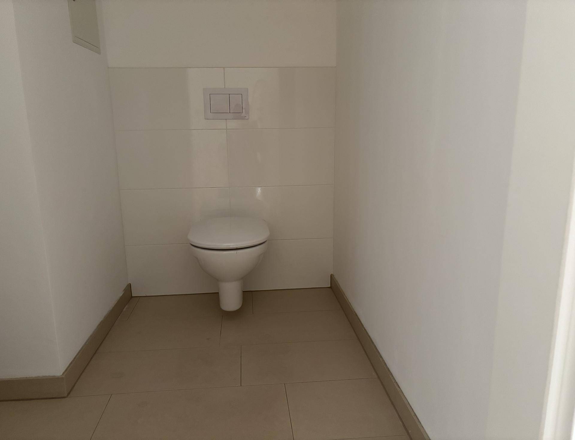 Separates WC mit wandhängender Toilette und hellen Fliesen am Boden und an der Wand.