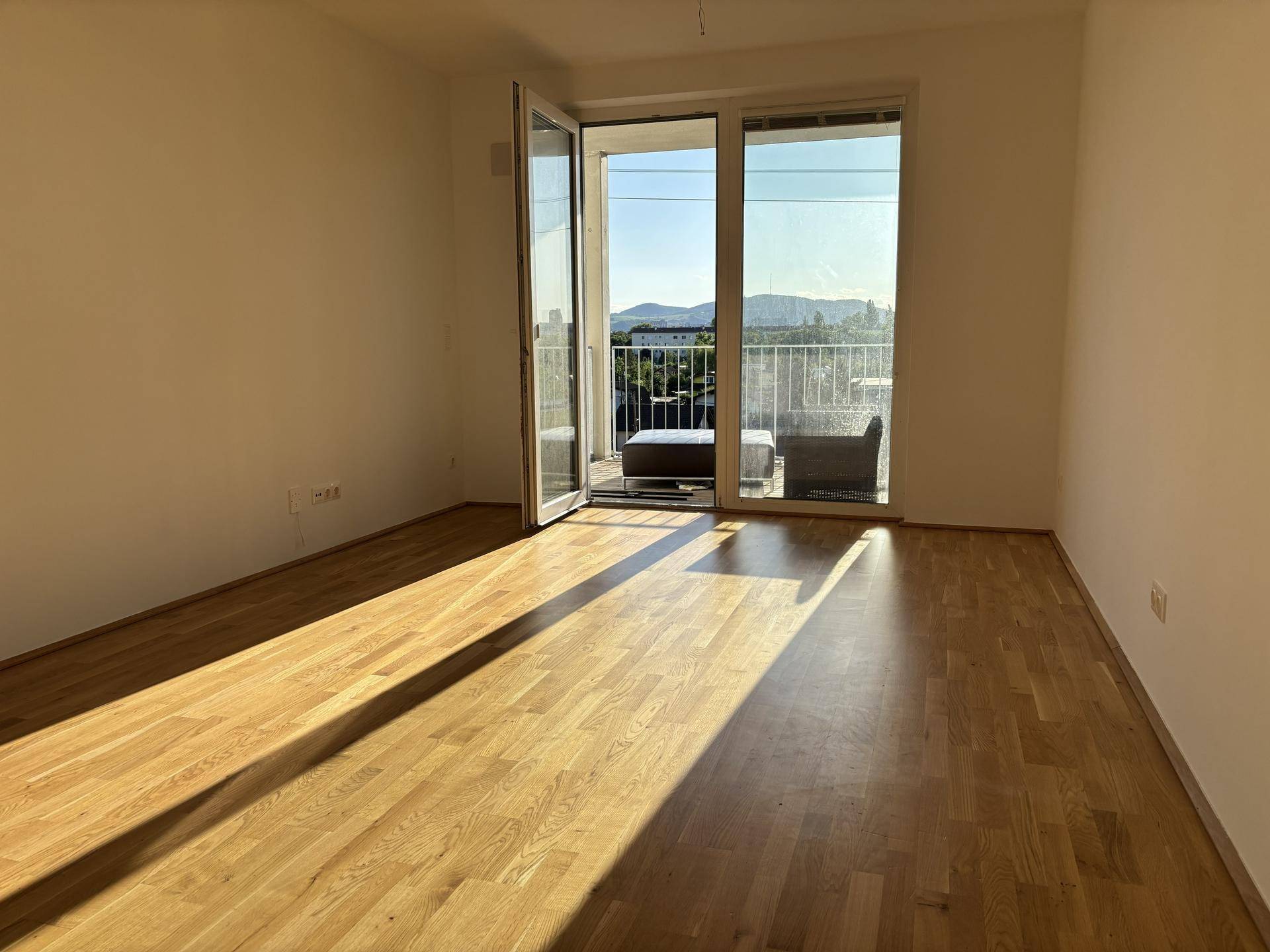Heller Wohnraum mit Eichenparkettboden und Zugang zu einem sonnigen Balkon.