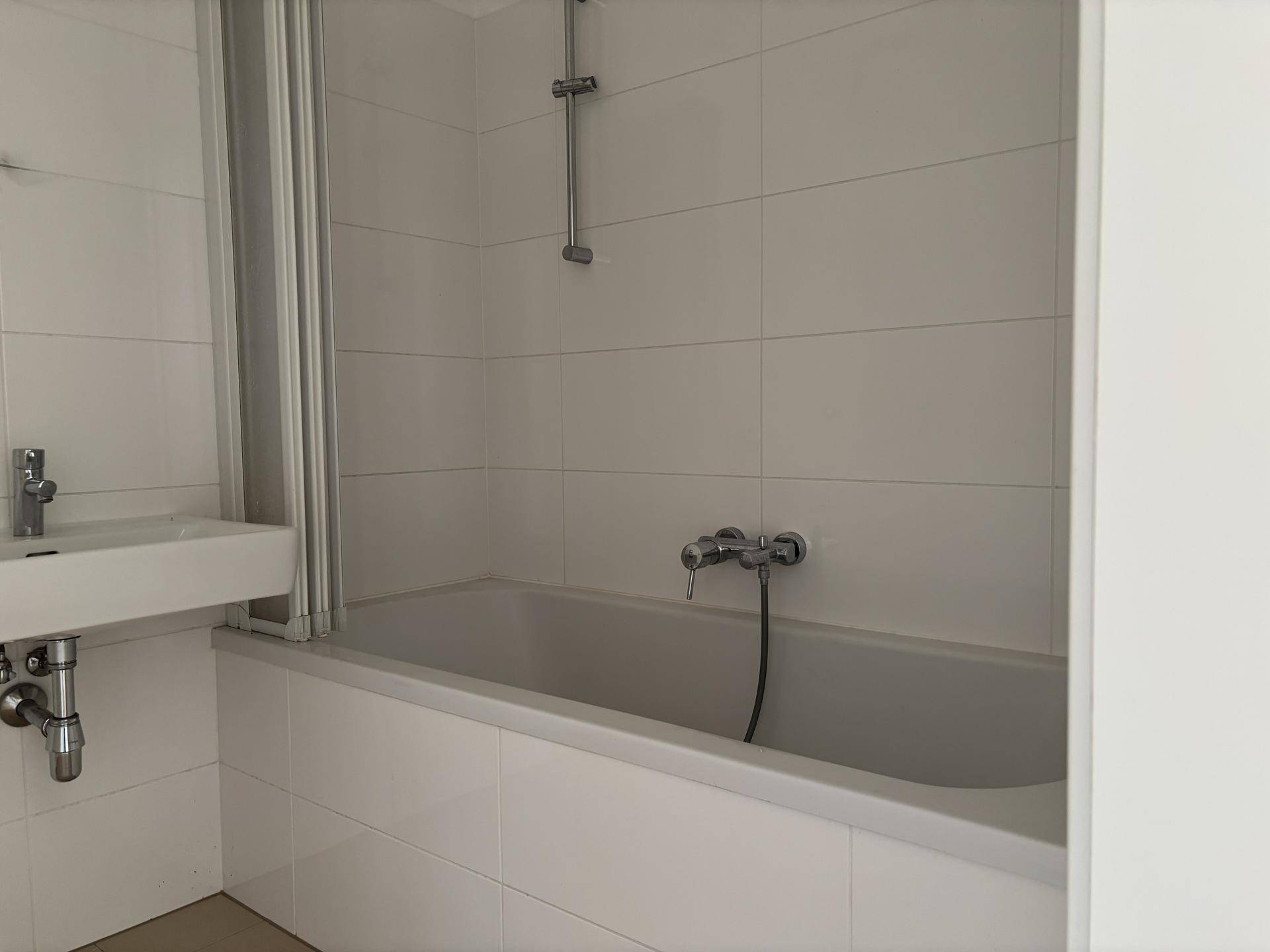 Badezimmer mit Badewanne, Duschabtrennung und weißen Fliesen an den Wänden.