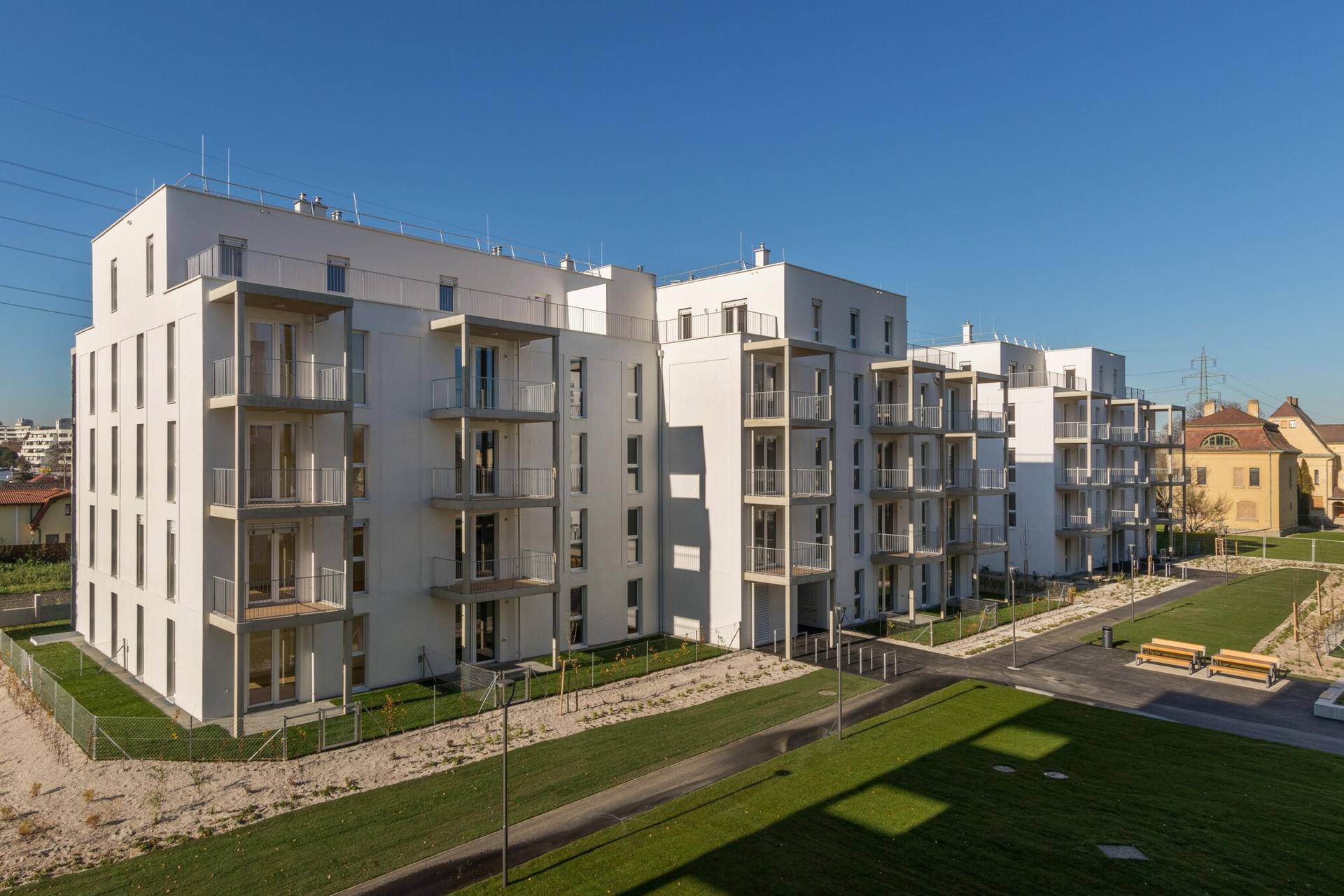 Moderne Wohnanlage mit weißer Fassade, zahlreichen Balkonen und gepflegten Grünflächen.