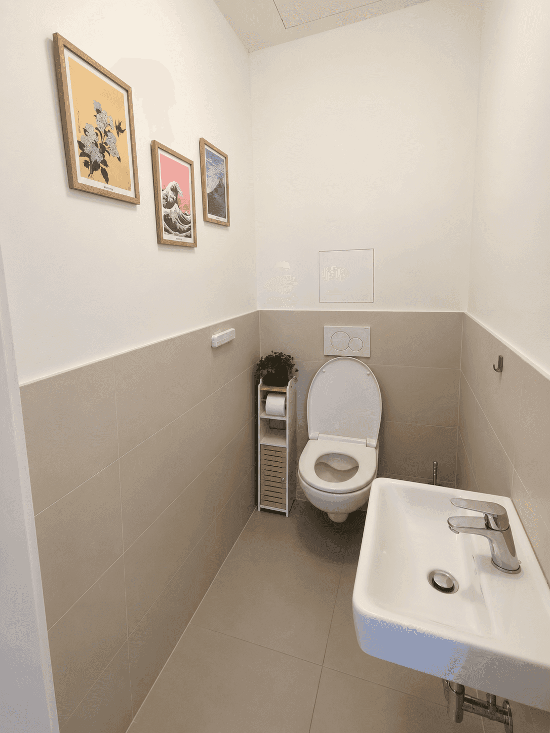 Gäste-WC mit wandhängender Toilette, kleinem Waschbecken und modernen Fliesen.