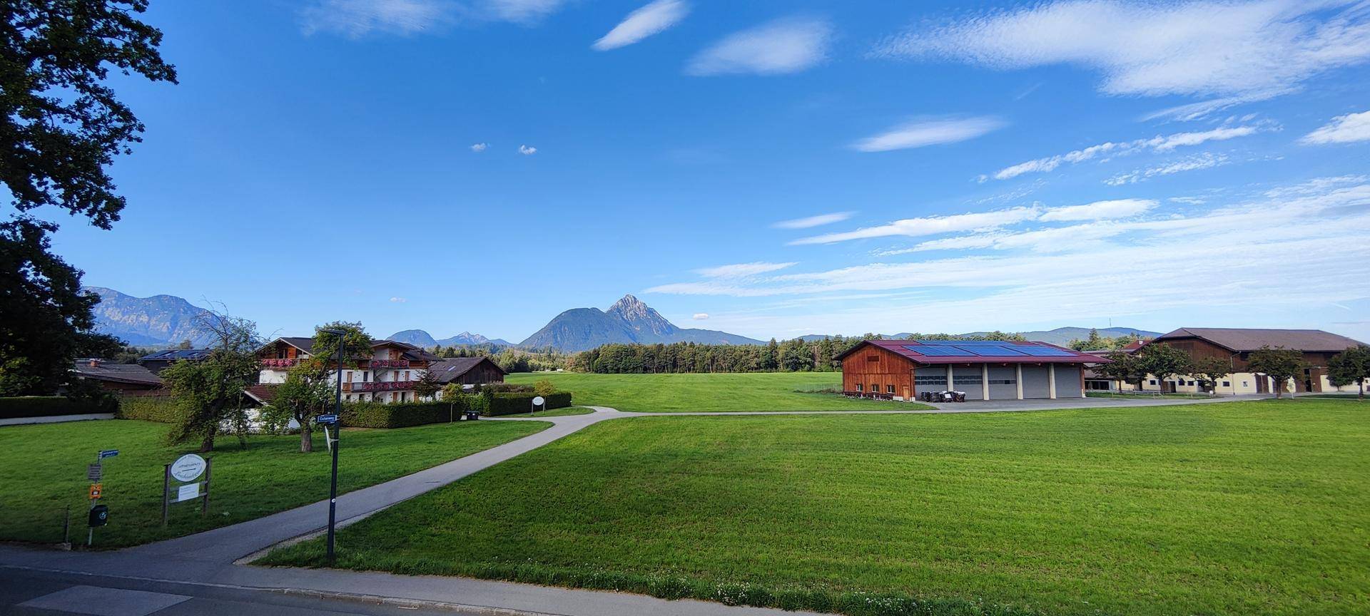 Weitläufige grüne Landschaft mit Bergen im Hintergrund und ländlicher Bebauung.