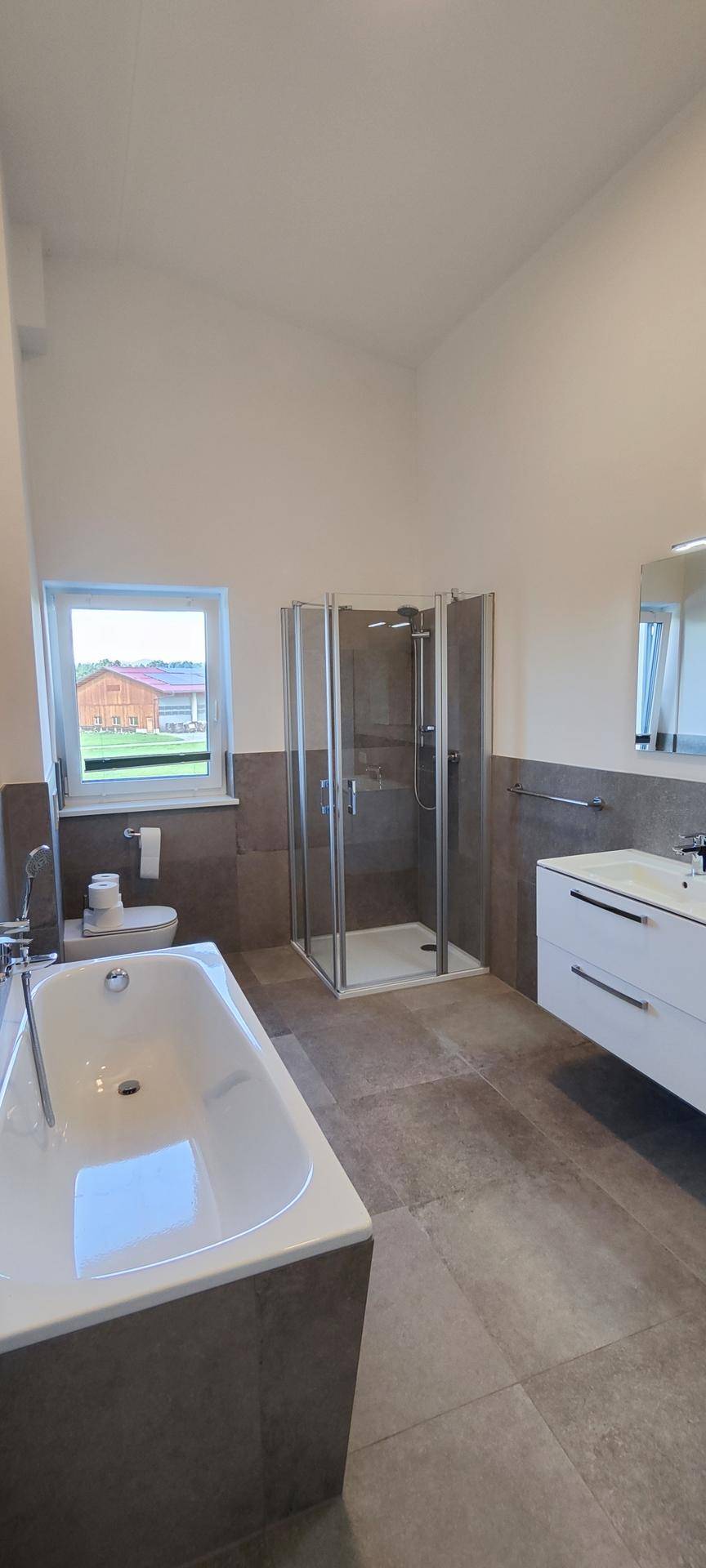 Helles Badezimmer mit Badewanne, Duschkabine und Fenster für Tageslicht.