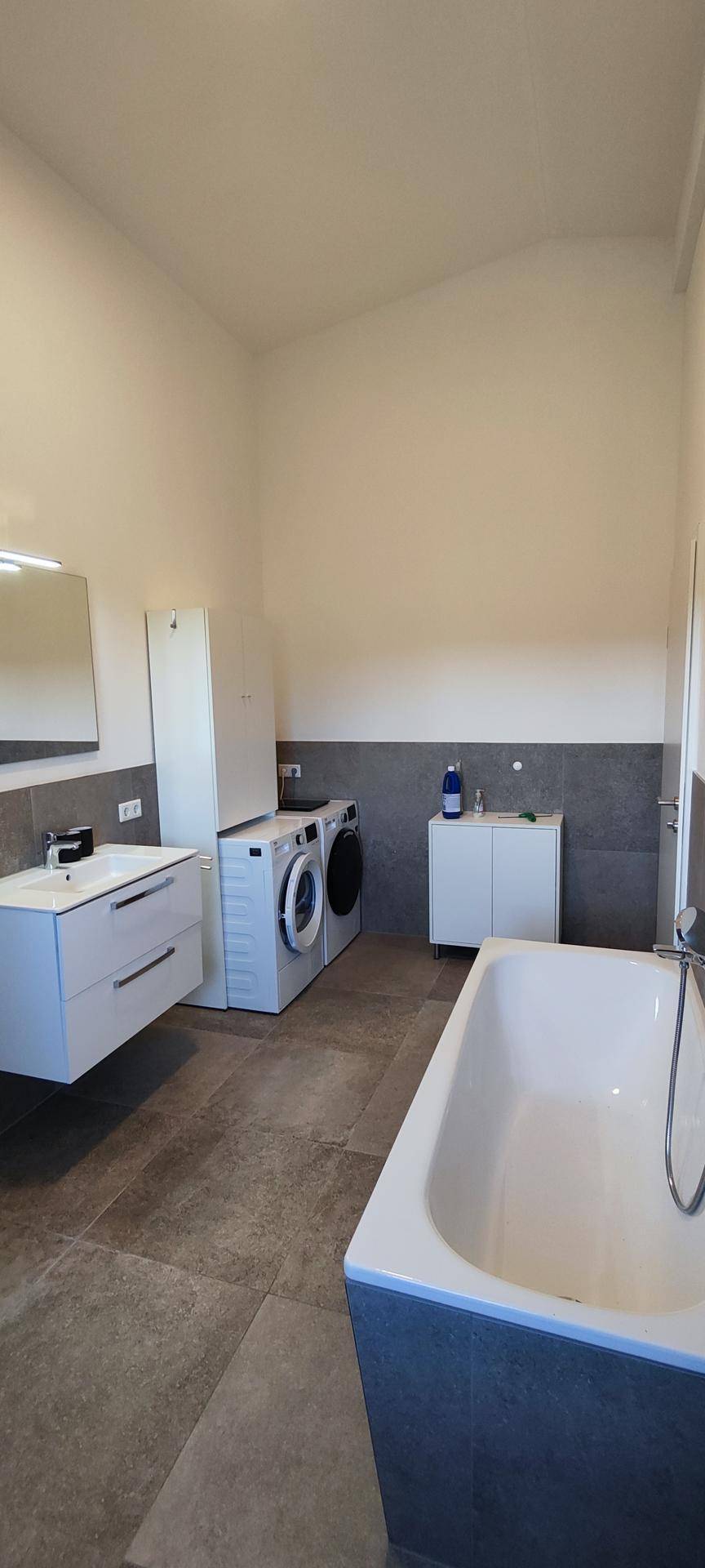 Geräumiges Badezimmer mit Badewanne, Waschmaschine und Trockner sowie Fliesenboden.