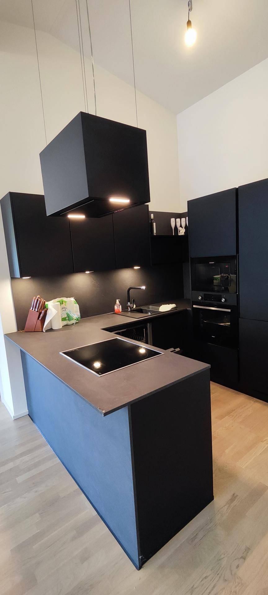 Moderne schwarze Einbauküche mit Kochinsel, Induktionskochfeld und integrierten Geräten.