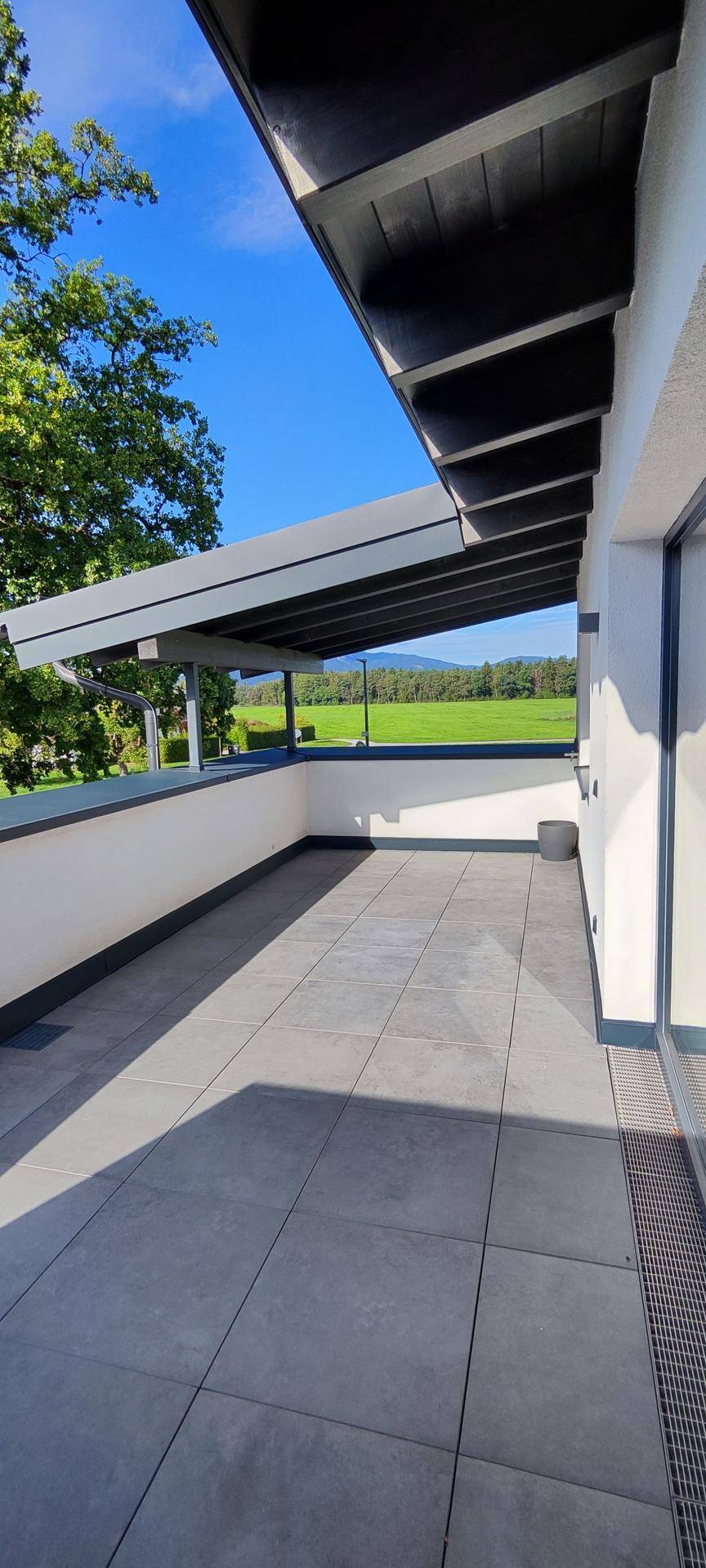 Geräumiger Balkon mit Fliesenboden und weitem Blick über die grüne Landschaft.