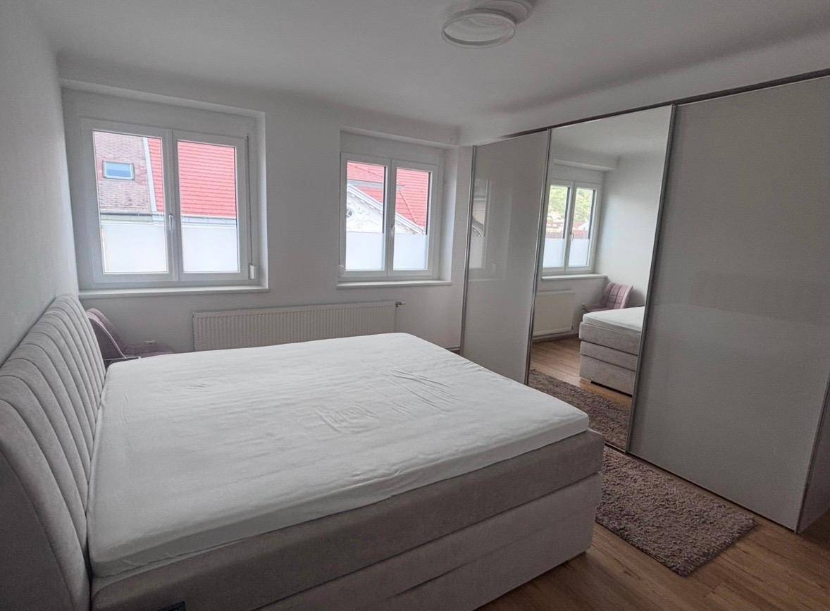 Schlafzimmer mit großem Bett, Spiegelschränken und zwei Fenstern, die den Raum erhellen.