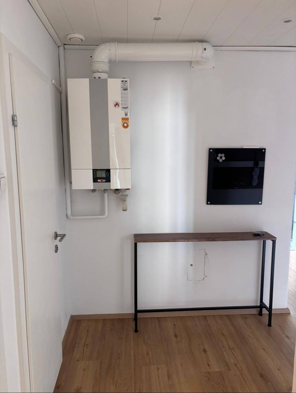Hauswirtschaftsraum mit Warmwasserbereiter, kleinem Konsolentisch und hellem Laminatboden.