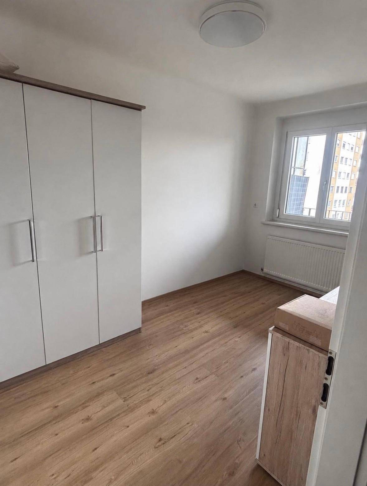 Helles Schlafzimmer mit weißem Kleiderschrank, Laminatboden und Fenster mit Blick auf die Umgebung.