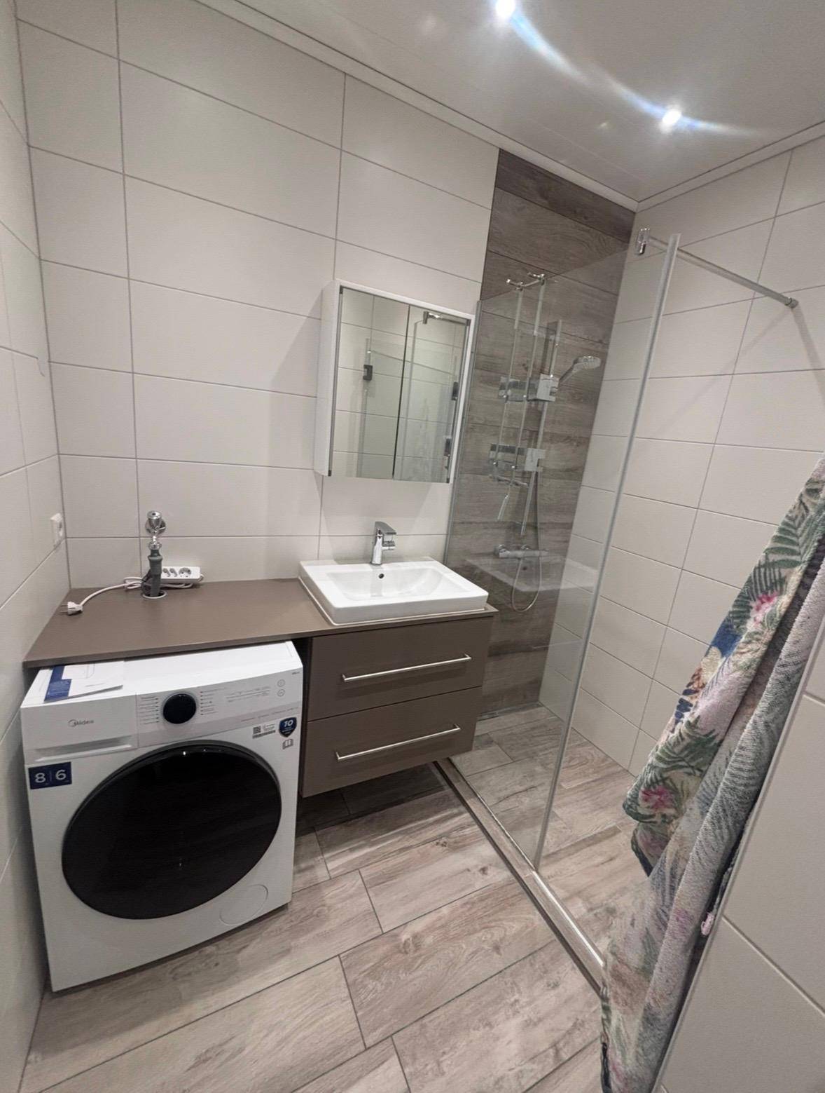 Modernes Badezimmer mit Duschkabine, Waschbeckenunterschrank und integrierter Waschmaschine.