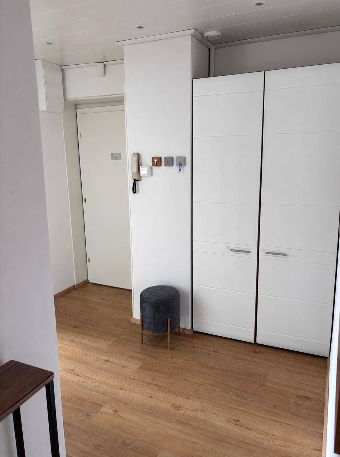 Heller Eingangsbereich mit weißem Kleiderschrank, Holzboden und Gegensprechanlage an der Wand.
