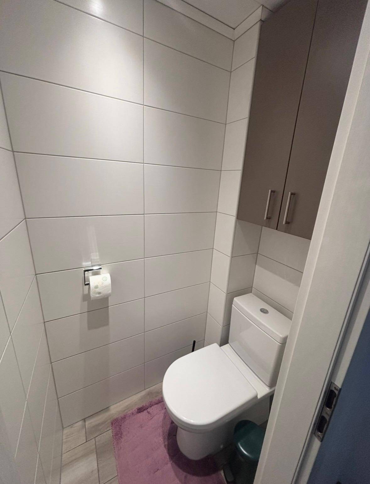 Separates WC mit Wandtoilette, Fliesenboden und praktischen Hängeschränken.