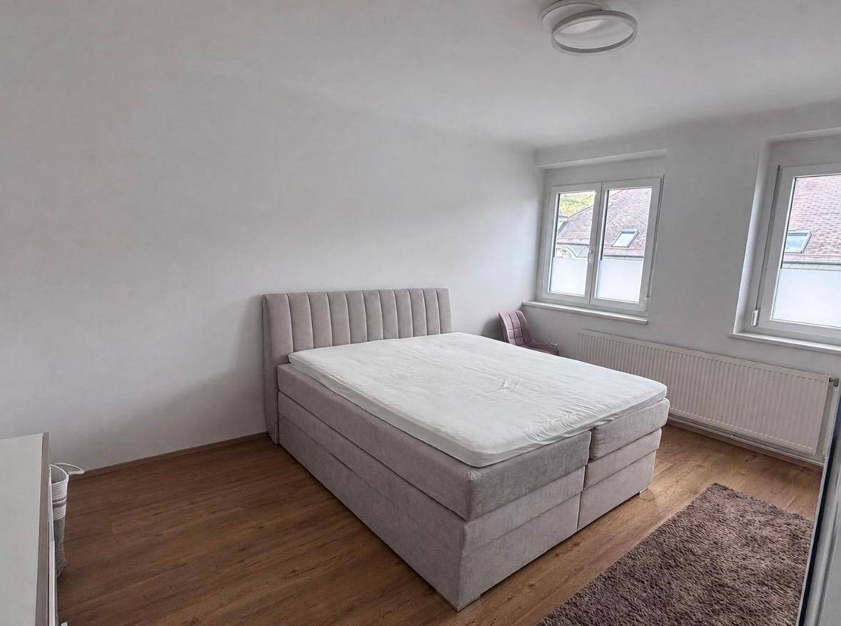 Gemütliches Schlafzimmer mit großem Boxspringbett, Teppich und zwei Fenstern für viel Tageslicht.