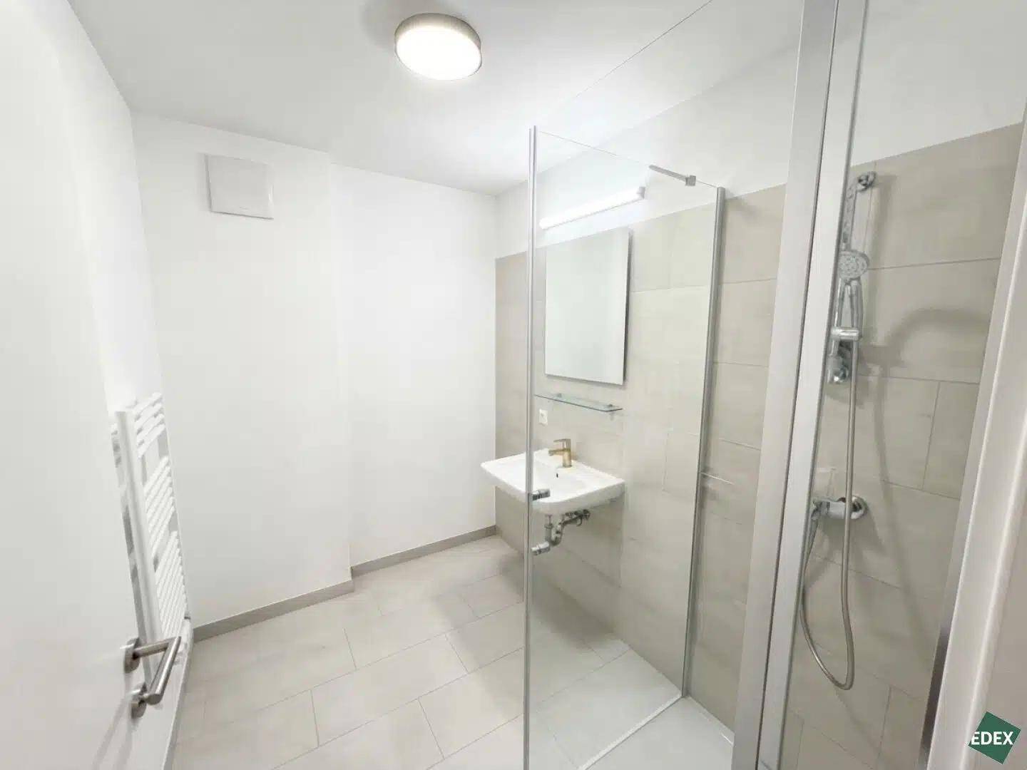 Modernes Badezimmer mit Dusche, Waschbecken, Spiegel und beheiztem Handtuchhalter.