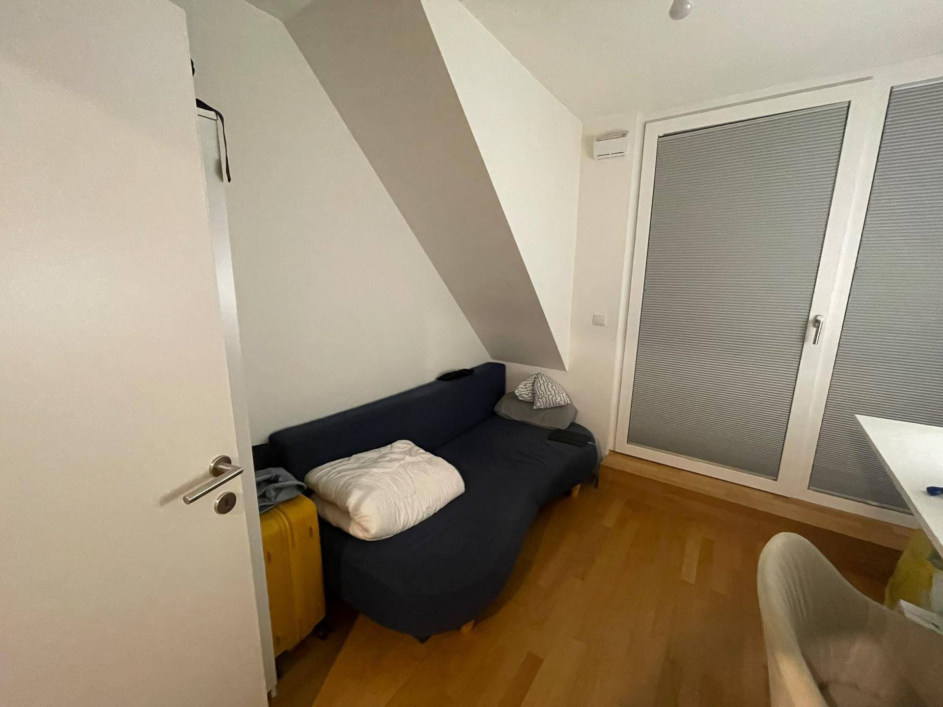 Helles Dachzimmer mit großem Fenster, Sofa und schräger Decke, bietet viel Tageslicht.