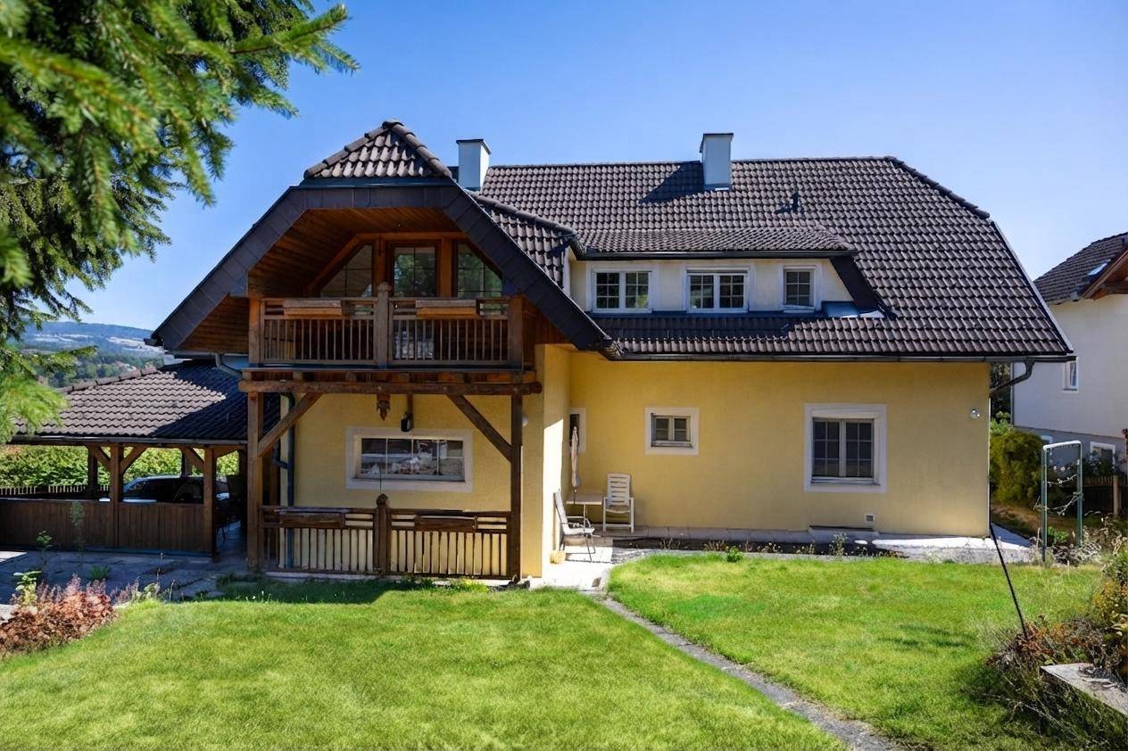 Rückseite des Hauses mit großem Holzbalkon, Carport und weitläufigem Gartenbereich.
