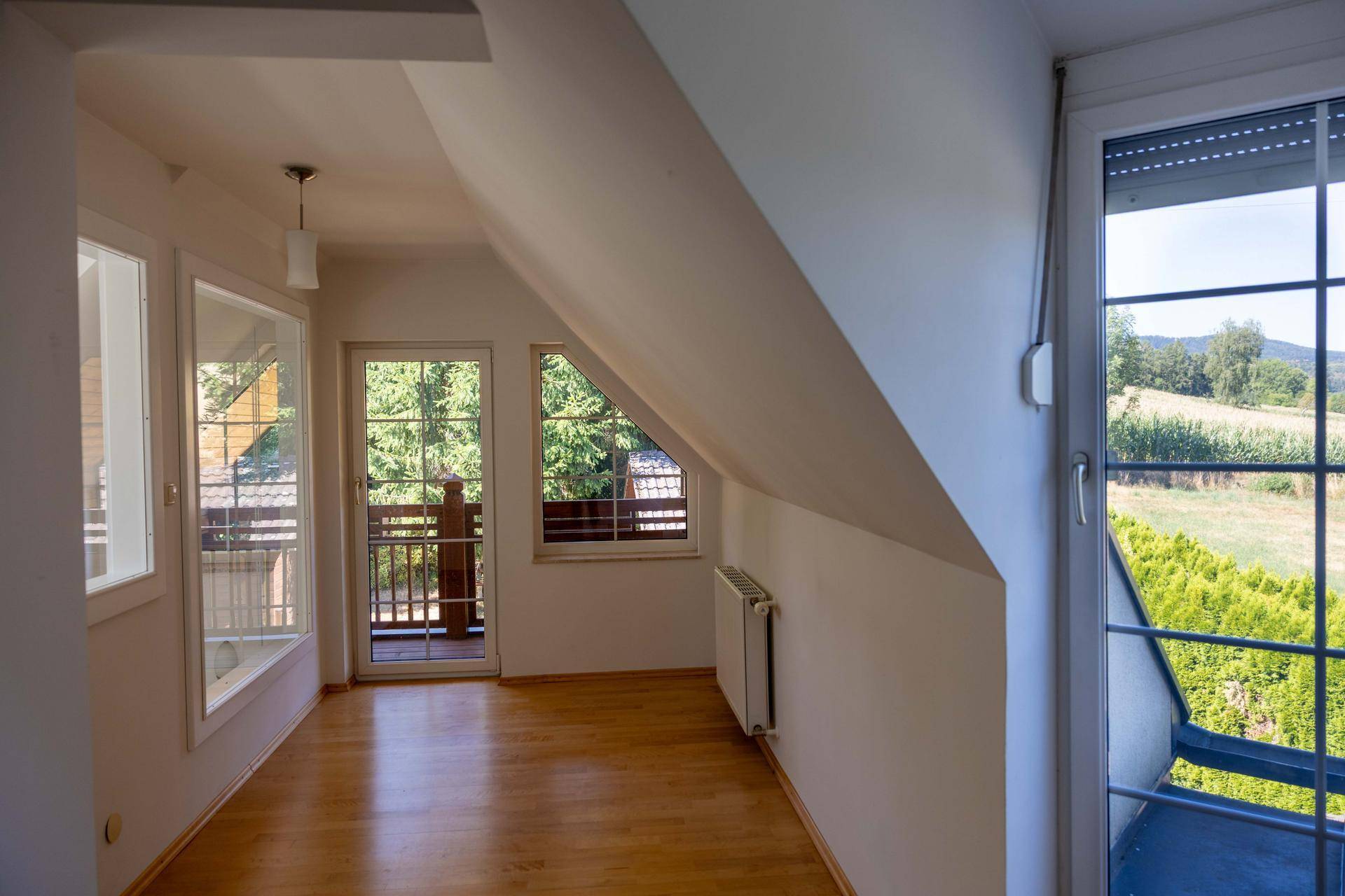 Heller Dachgeschossraum mit schrägen Wänden, Holzboden und Zugang zu einem kleinen Balkon.