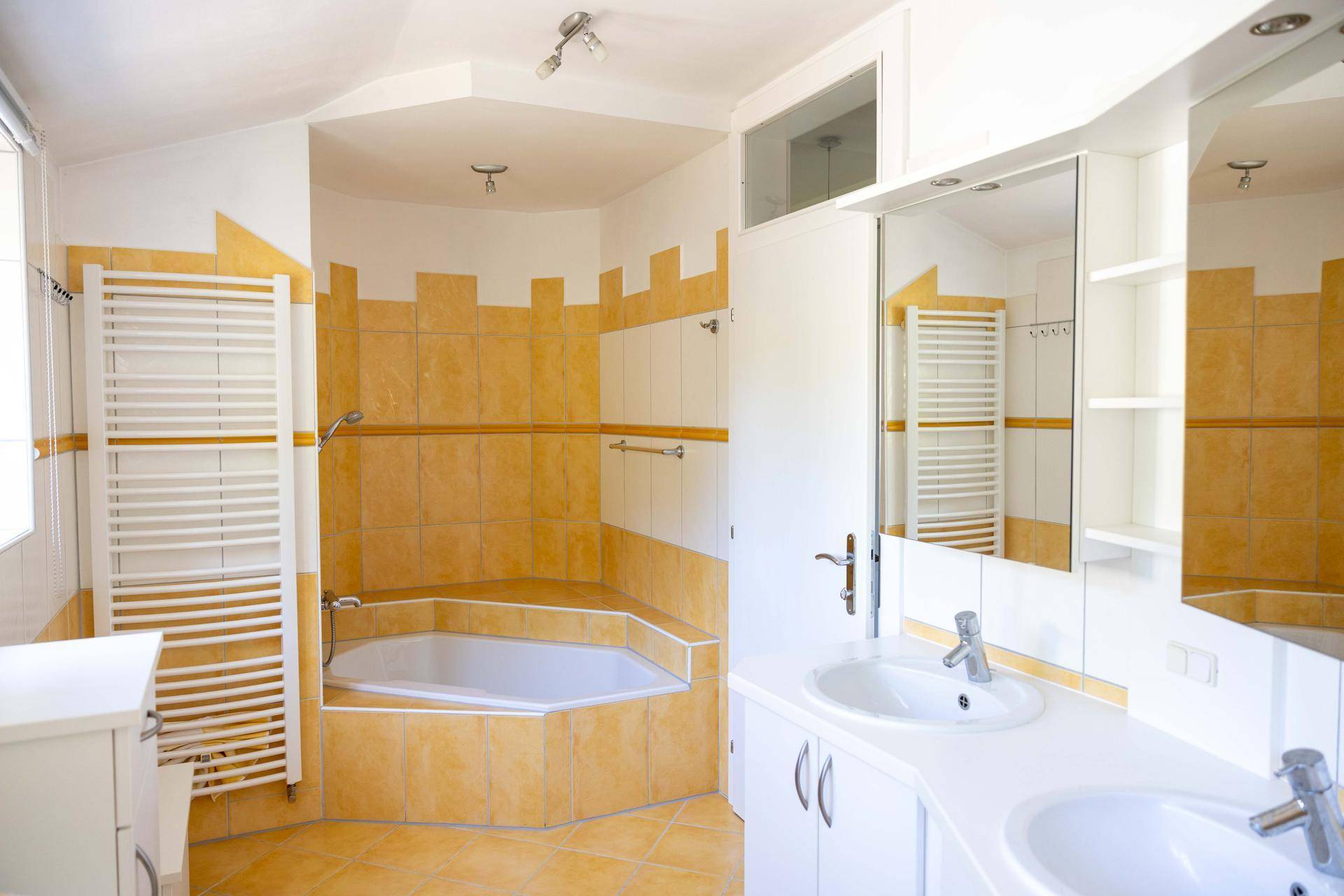 Geräumiges Badezimmer mit gelben Fliesen, Eckbadewanne, Doppelwaschbecken und Handtuchheizkörper.