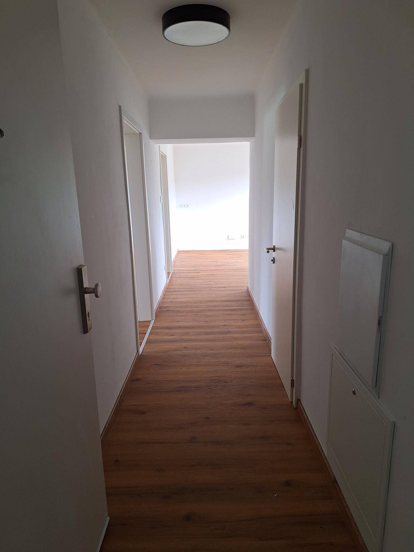 Langer, heller Flur mit Laminatboden, der zu verschiedenen Räumen der Wohnung führt und gut gepflegt ist.