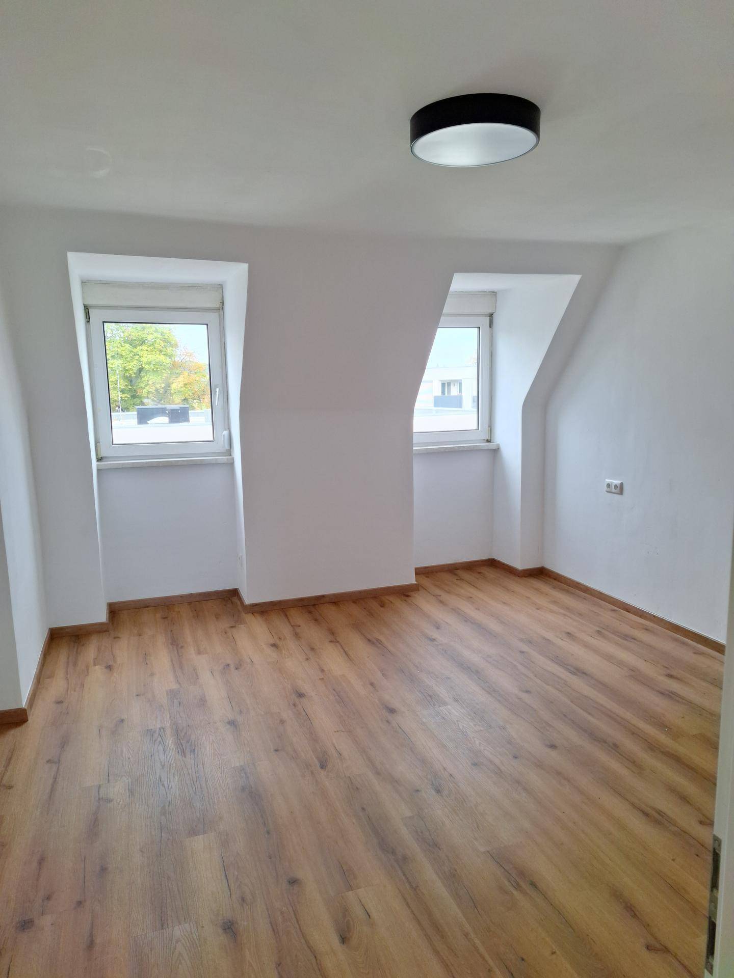 Geräumiges Dachgeschosszimmer mit hellem Laminatboden und schrägen Wänden, frisch renoviert und bezugsfertig.