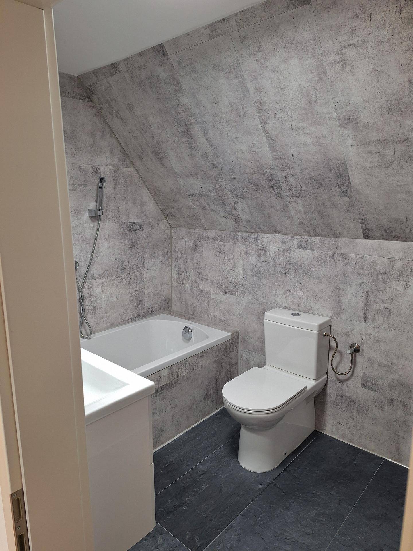 Modernes Badezimmer im Dachgeschoss mit Badewanne, WC und grauen Fliesen an Wänden und Boden, sehr gepflegt.