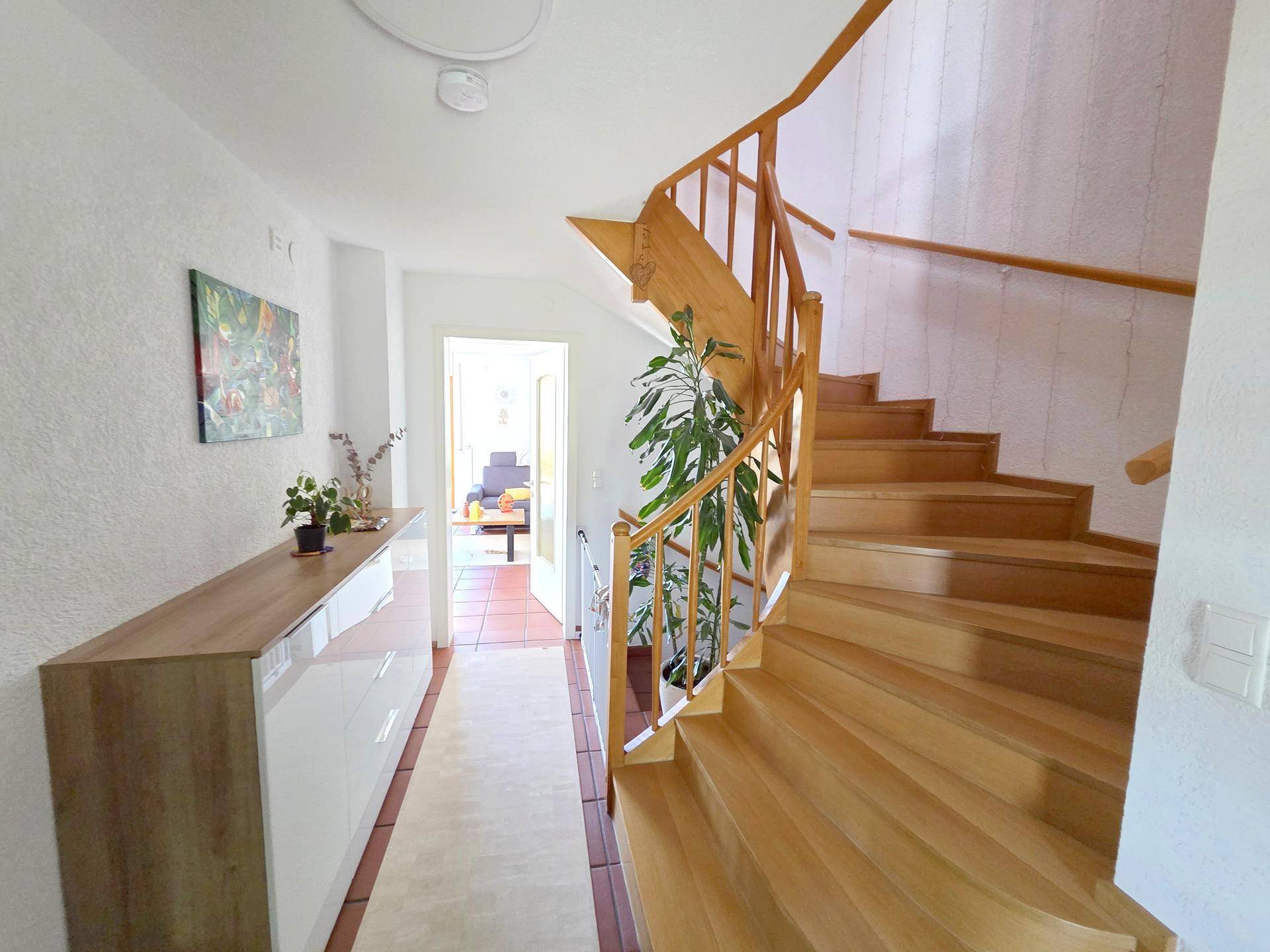 Heller Flur mit eleganter Holztreppe und modernem Sideboard, führt zu weiteren Räumen.
