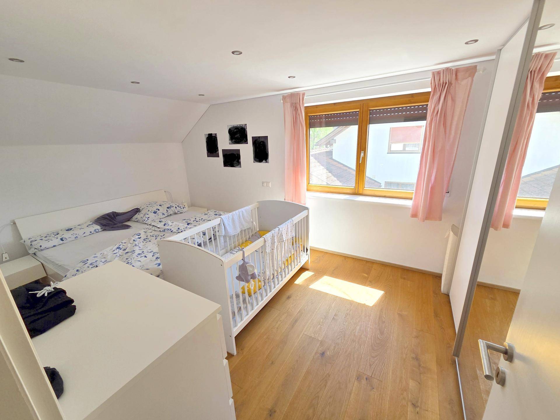 Gemütliches Schlafzimmer im Dachgeschoss mit Holzboden, Doppelbett und Babybett.