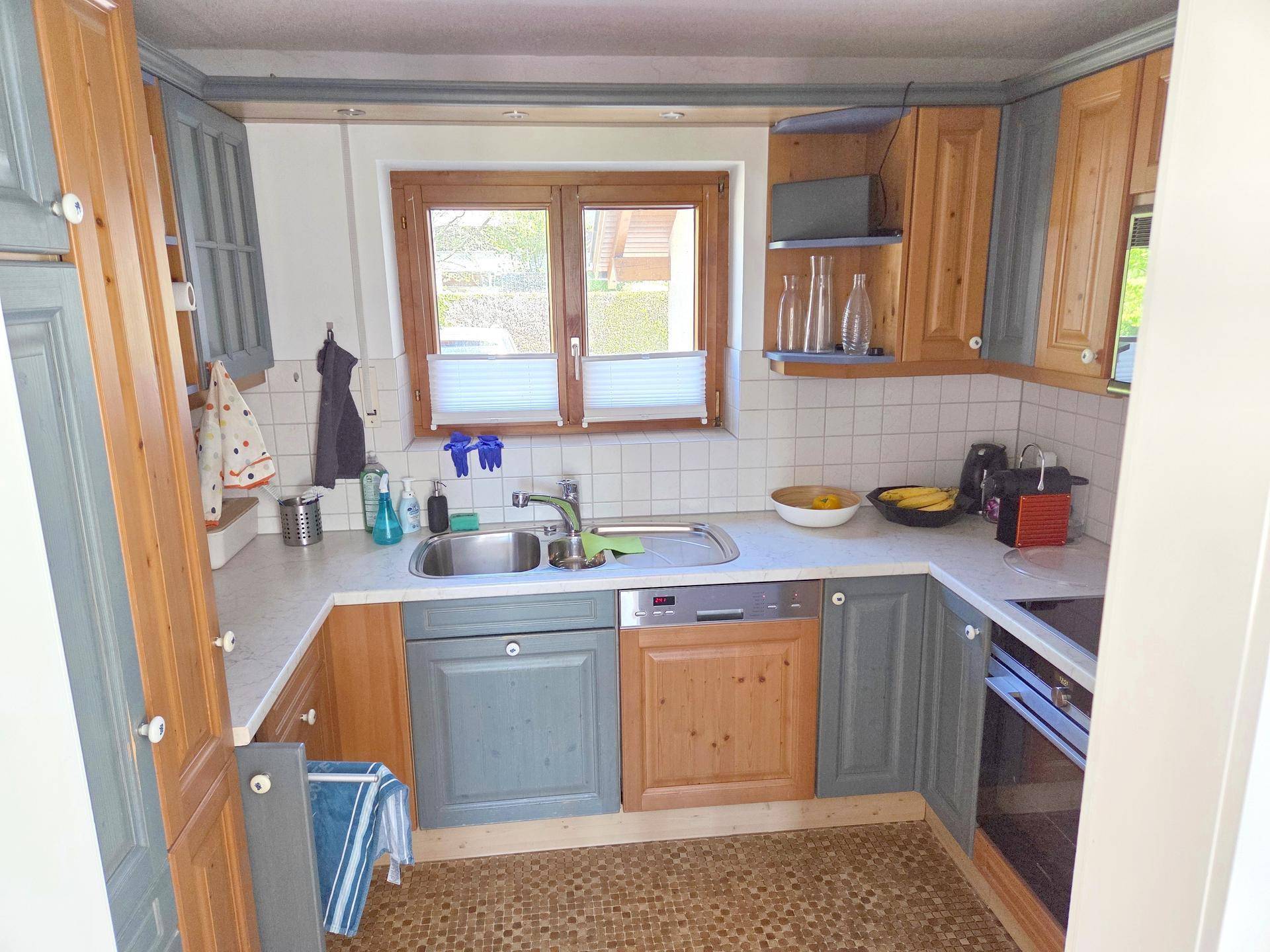 Funktionale Küche mit Holz- und grauen Schränken, Fenster und integriertem Geschirrspüler.