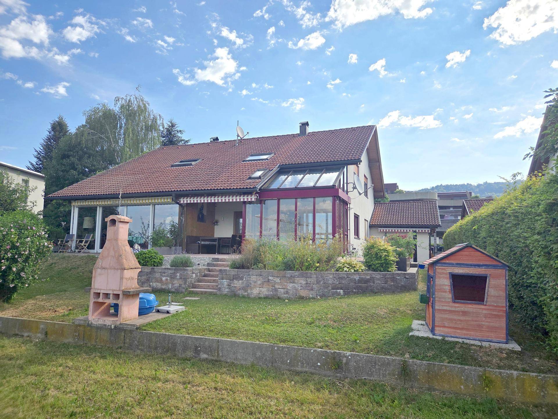 Rückansicht des Hauses mit weitläufigem Garten, Wintergarten und gemauertem Grillplatz.