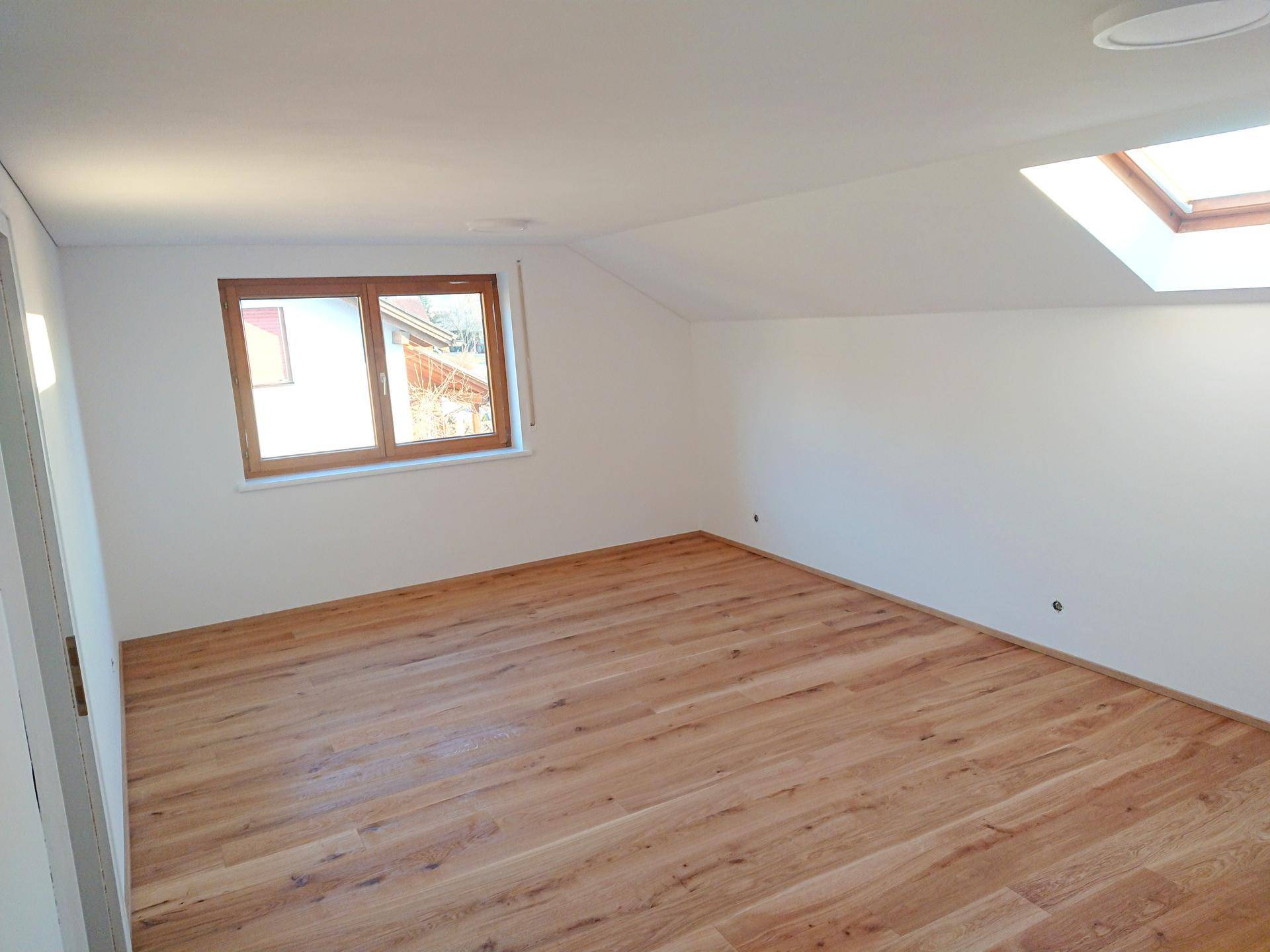 Helles Zimmer im Dachgeschoss mit neuem Holzboden, Fenster und Dachschräge.