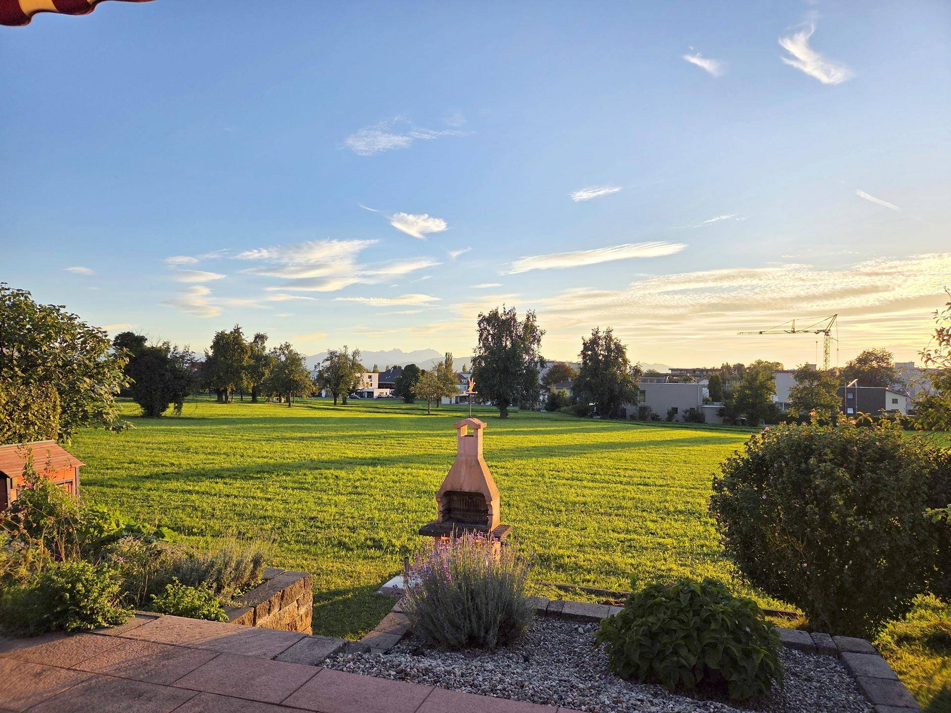 Weitläufiger Blick über grüne Felder bis zu den Bergen am Horizont bei Sonnenuntergang.