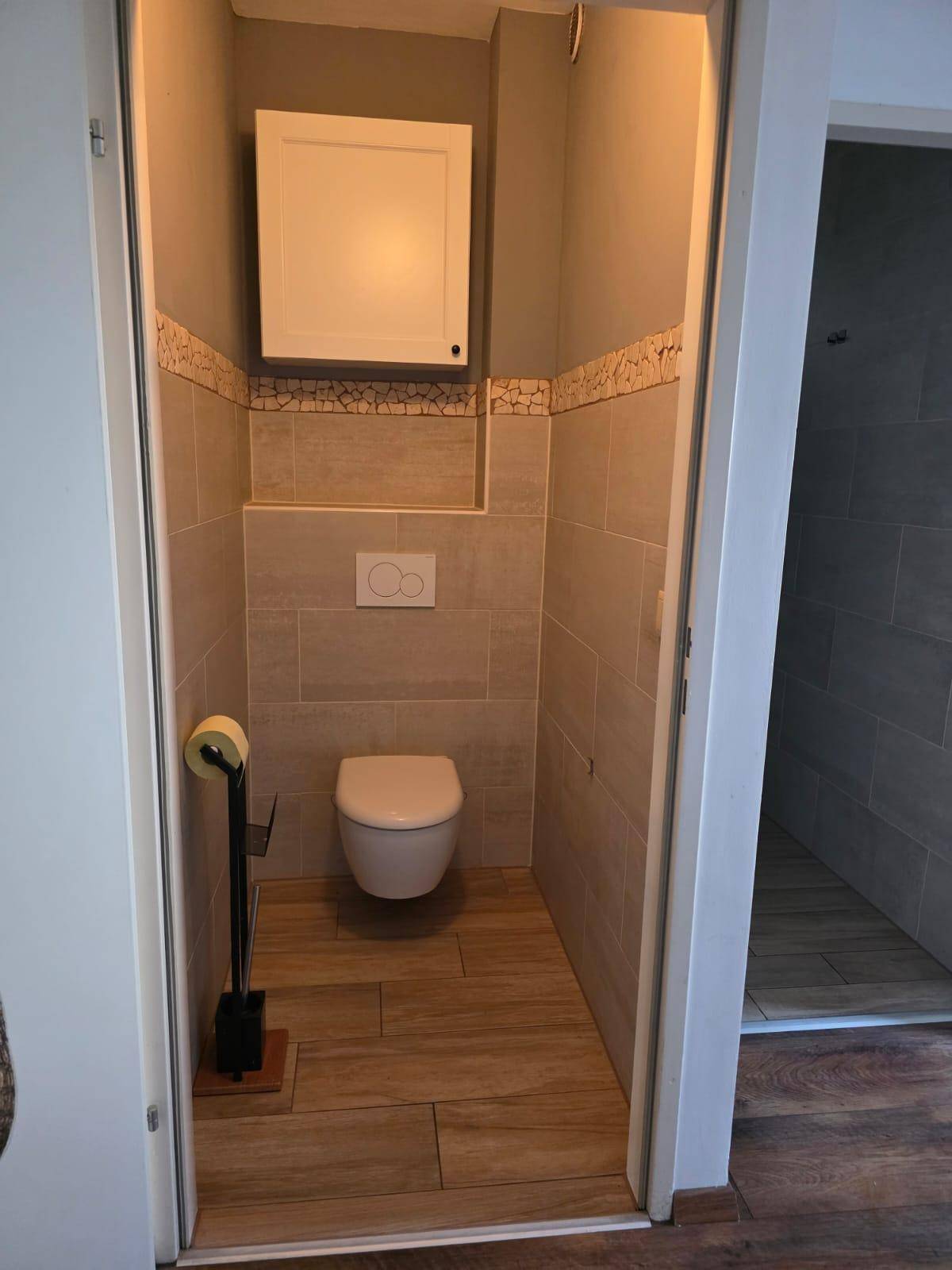 Gäste-WC mit wandhängender Toilette und modernen Fliesen an den Wänden.