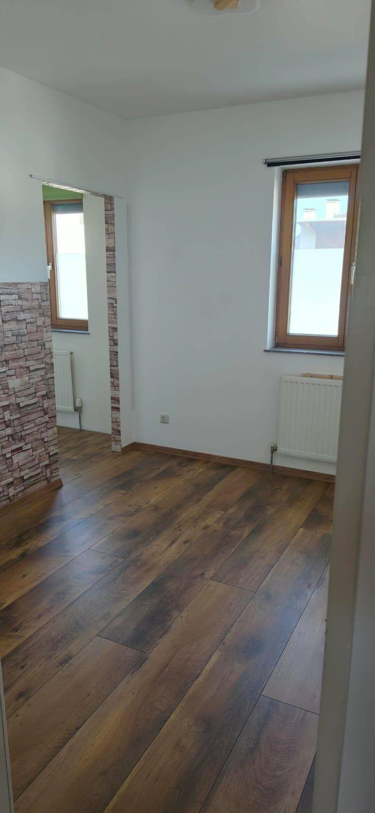 Heller Raum mit Laminatboden und Fenster, mit Blick in einen angrenzenden Bereich mit dekorativer Wandverkleidung.