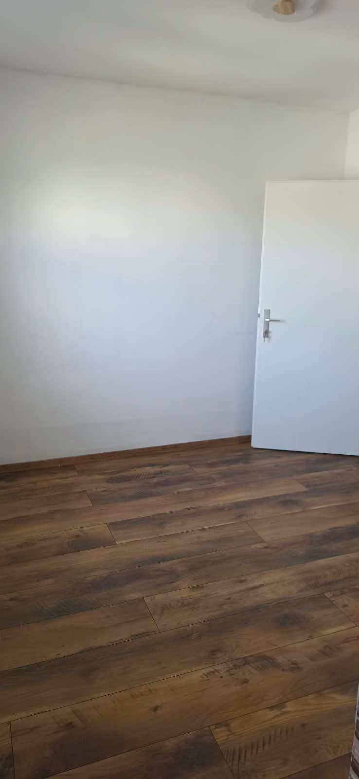 Leerer Raum mit Laminatboden und weiß gestrichenen Wänden, bereit zur individuellen Gestaltung.