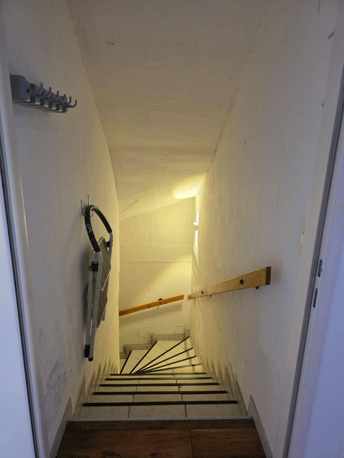Treppenabgang zum Keller mit weiß gestrichenen Wänden und Holzgeländer.