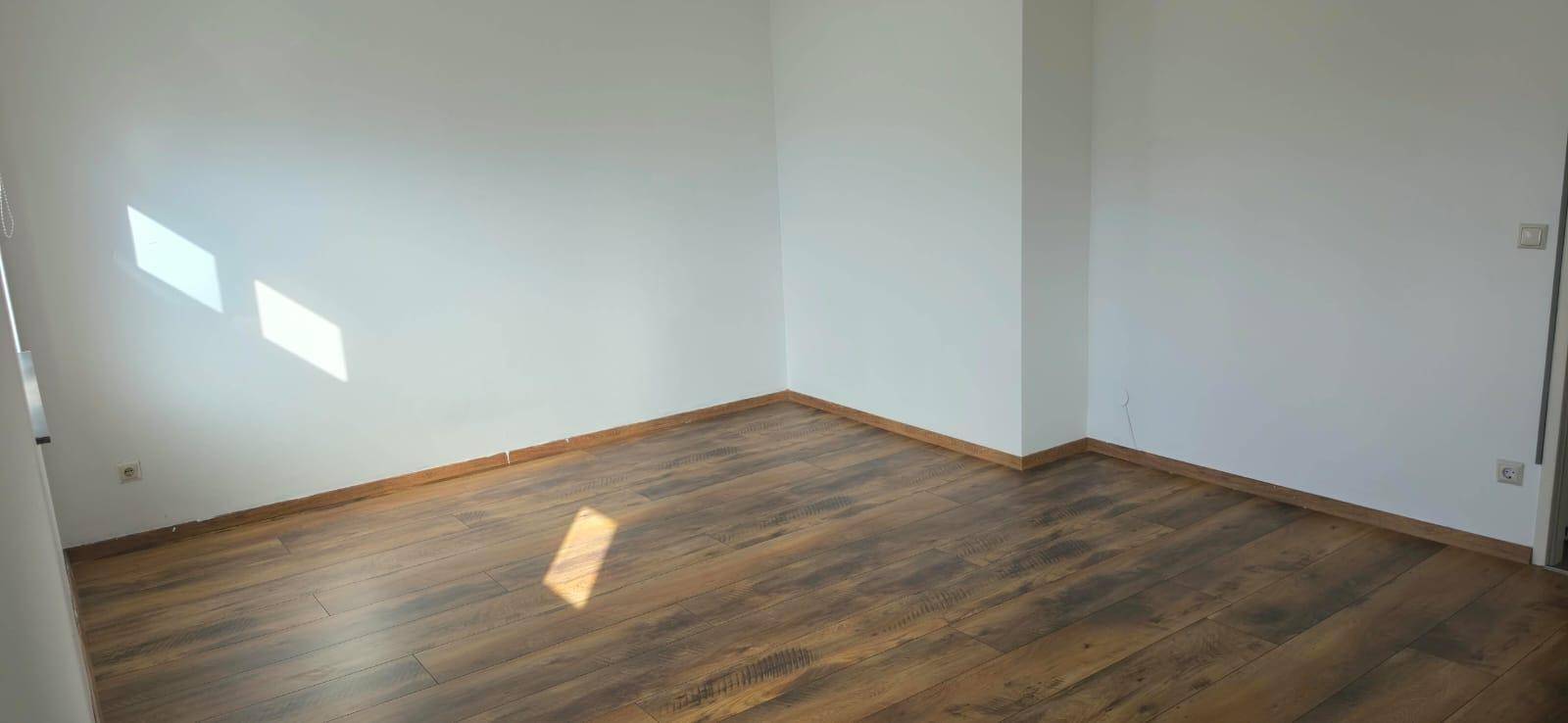 Heller, leerer Raum mit Laminatboden und weißen Wänden, durchflutet von natürlichem Sonnenlicht.