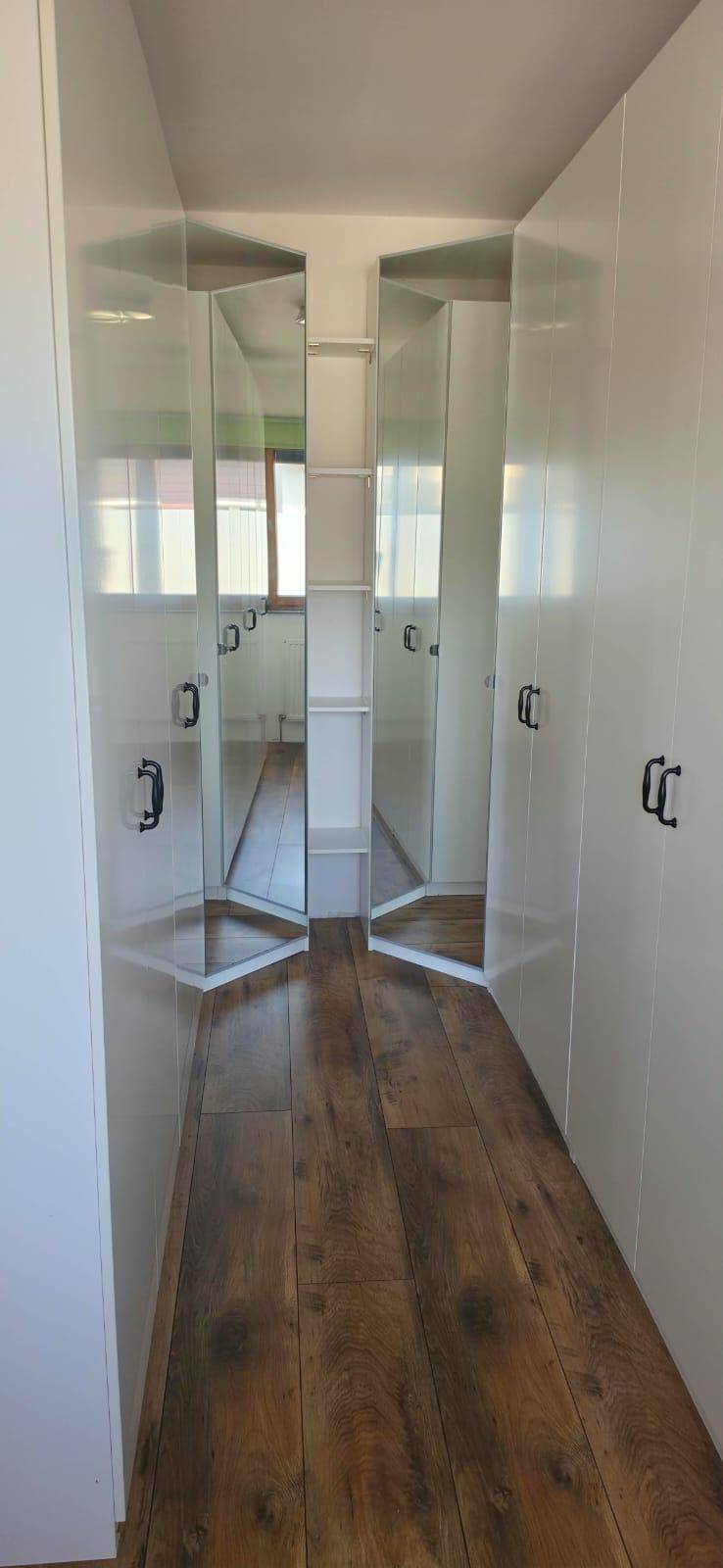 Begehbarer Kleiderschrank mit weißen Einbauschränken und Spiegeltüren, die den Raum optisch vergrößern.