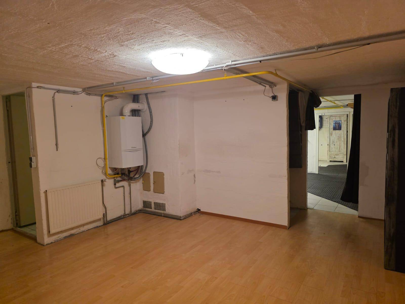 Hauswirtschaftsraum im Keller mit Heizungsanlage, freiliegenden Rohren und Laminatboden.