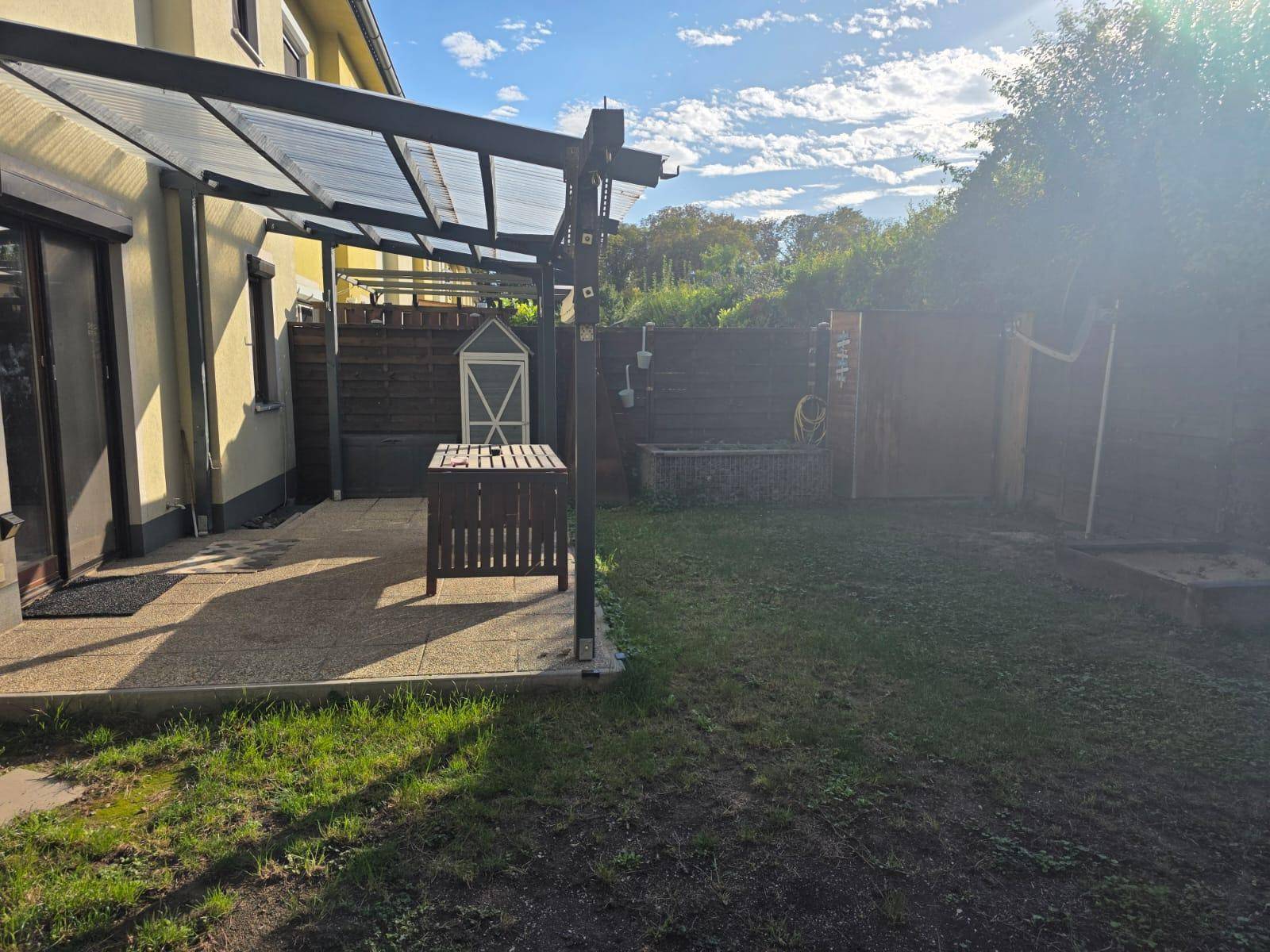 Sonniger Hinterhof mit überdachter Terrasse, Rasen und Holzzaun, ideal für entspannte Stunden im Freien.