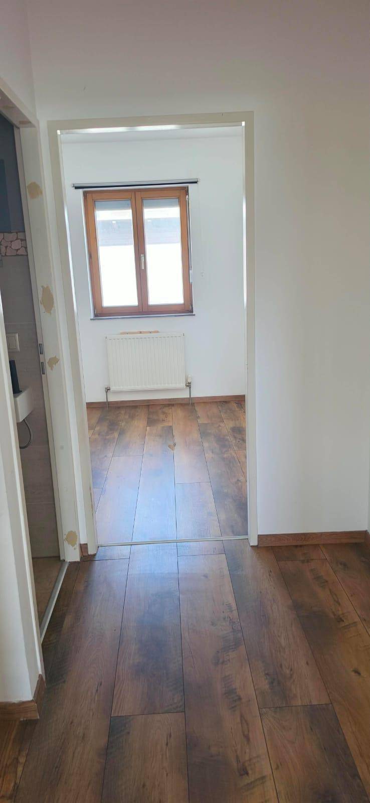 Blick vom Flur in einen Raum mit Laminatboden und einem Fenster, das Tageslicht spendet.