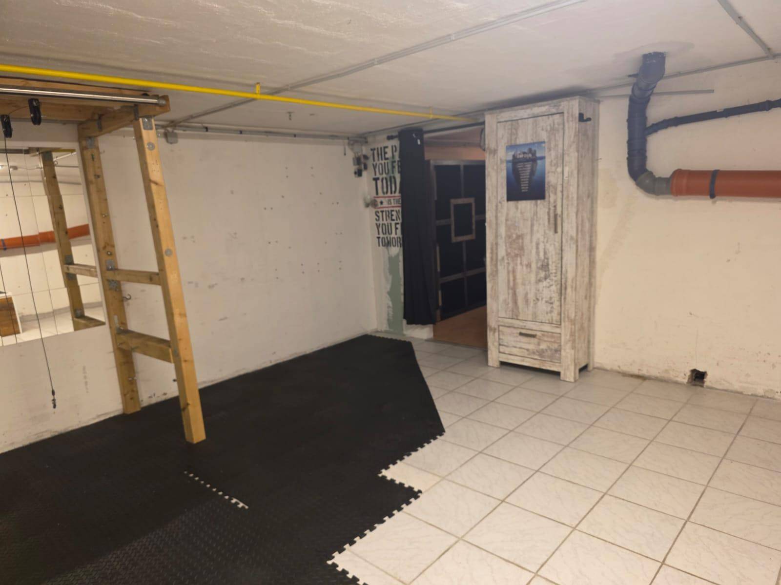 Kellerraum, teilweise als Fitnessbereich genutzt, mit Fliesen und Gummimattenboden.