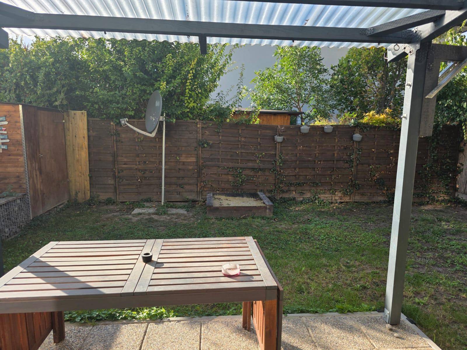 Überdachte Terrasse mit Holztisch und Blick auf den Garten mit einem kleinen Sandkasten.