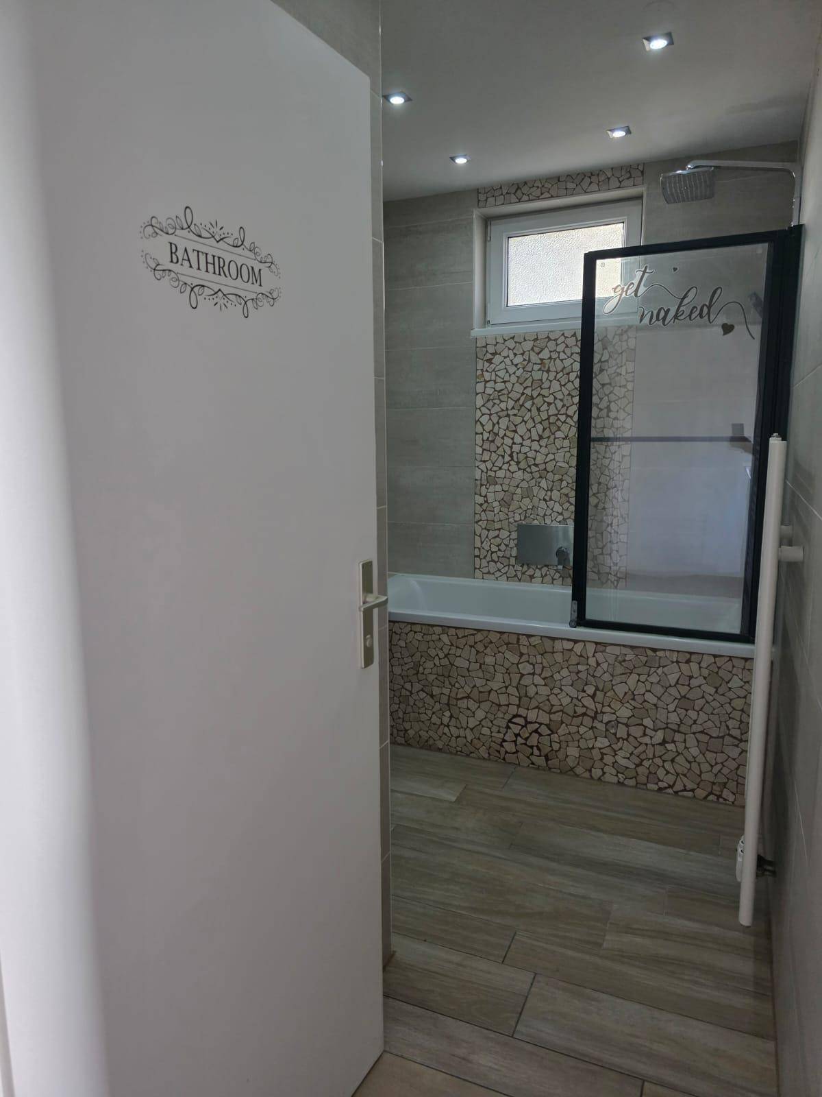 Helles Badezimmer mit Badewanne, Duschwand, Fenster und beheiztem Handtuchhalter.