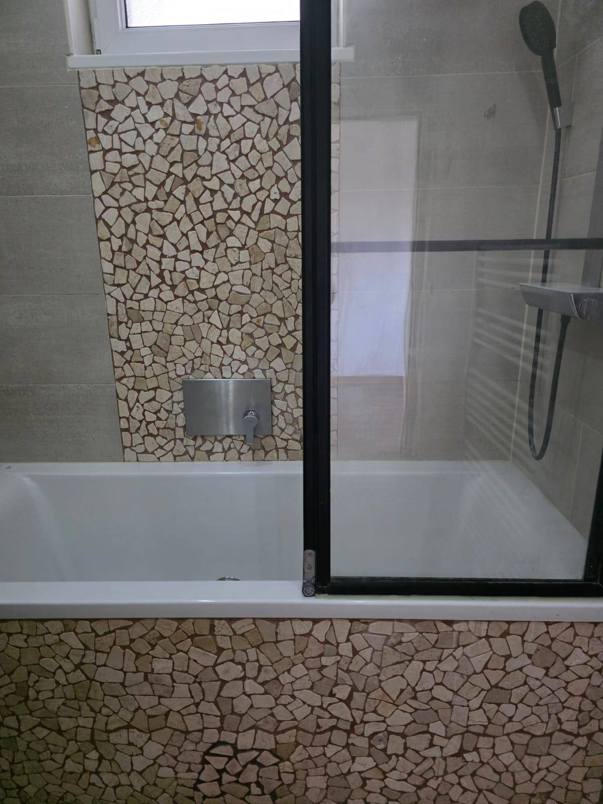 Badezimmer mit Badewanne, Duschwand und dekorativen Mosaikfliesen.