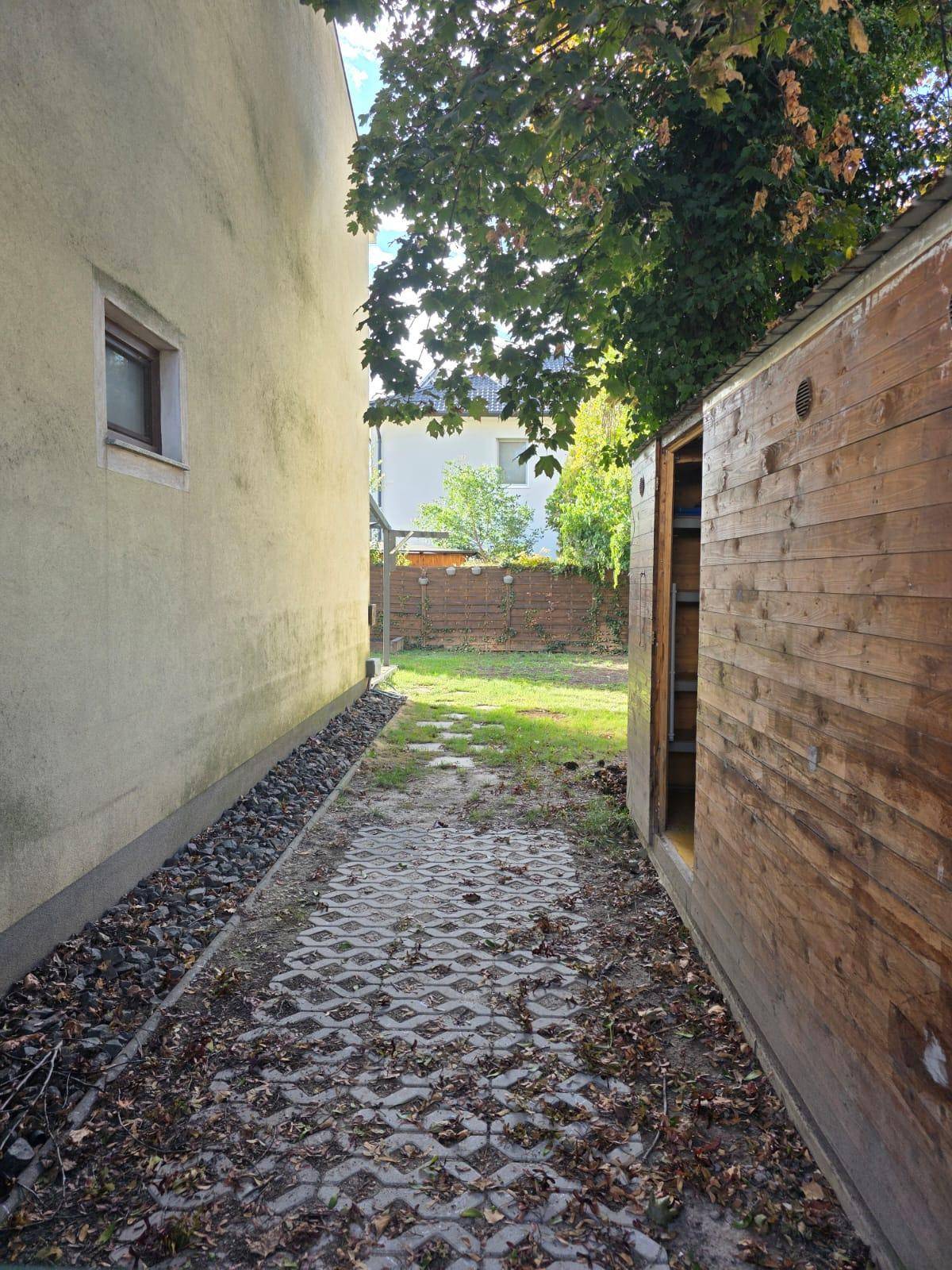 Seitenweg zwischen zwei Gebäuden, der zu einer Rasenfläche und einem Holzschuppen führt.