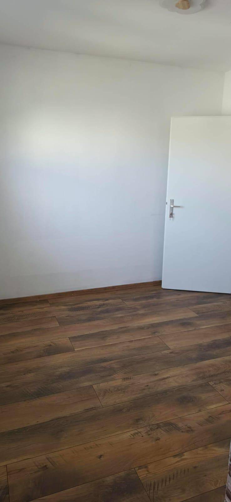 Leerer Raum mit Laminatboden und weiß gestrichenen Wänden, bereit zur individuellen Gestaltung.