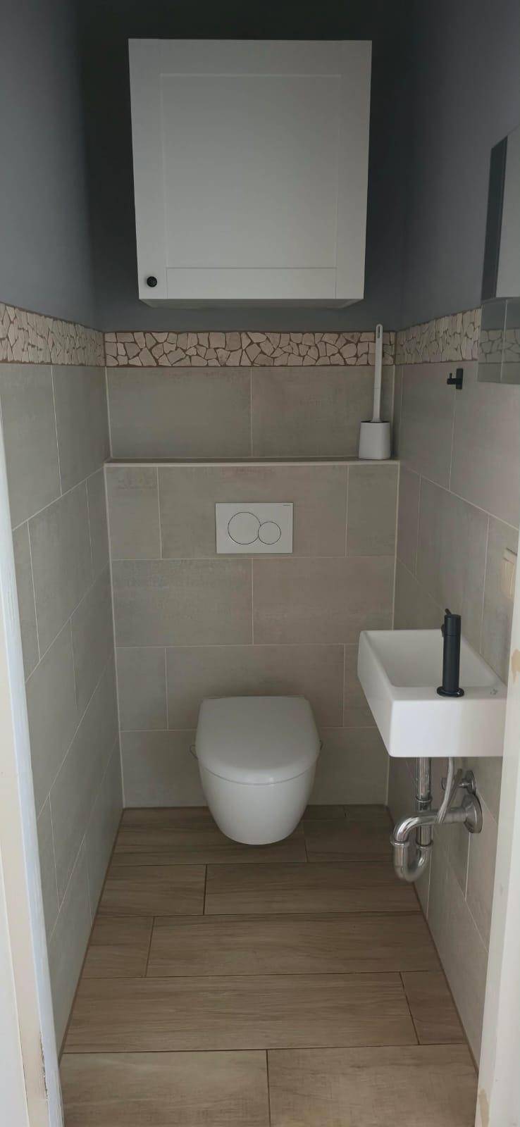 Detailansicht des Gäste-WCs mit modernen Fliesen, Wand-WC und einem praktischen Waschbecken.