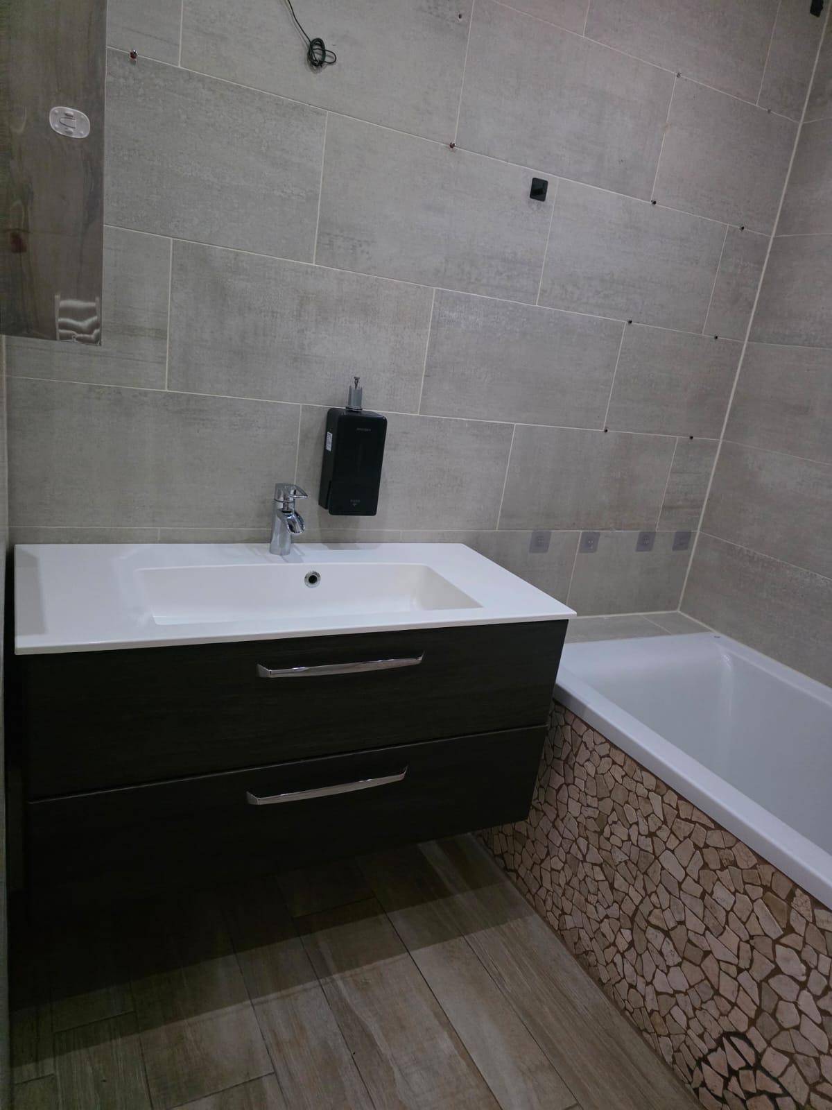 Badezimmer mit modernem Waschtisch, Einzelwaschbecken und Badewanne, gefliest in Grau.