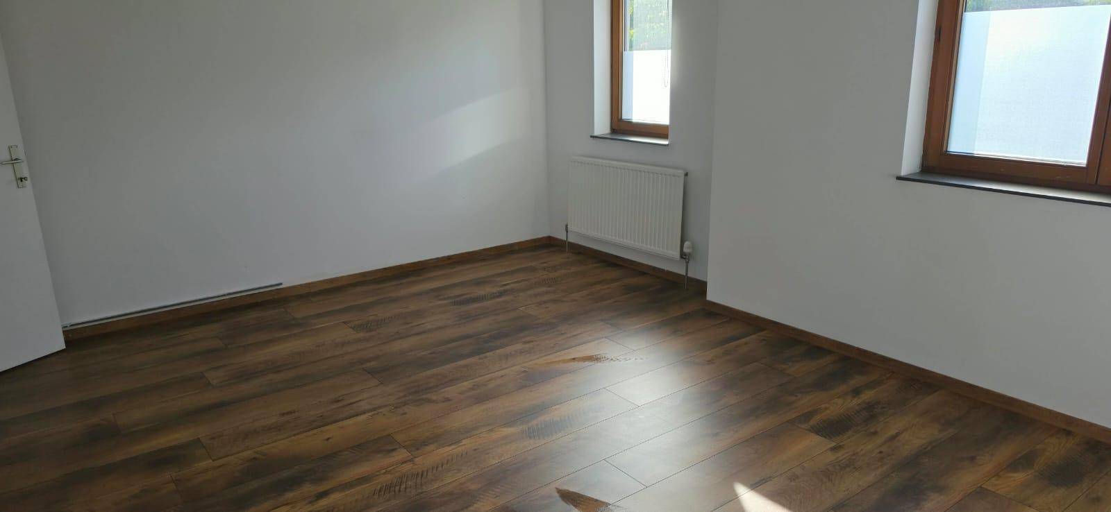 Heller Raum mit Laminatboden, zwei Fenstern und einem Heizkörper, der für eine angenehme Wärme sorgt.