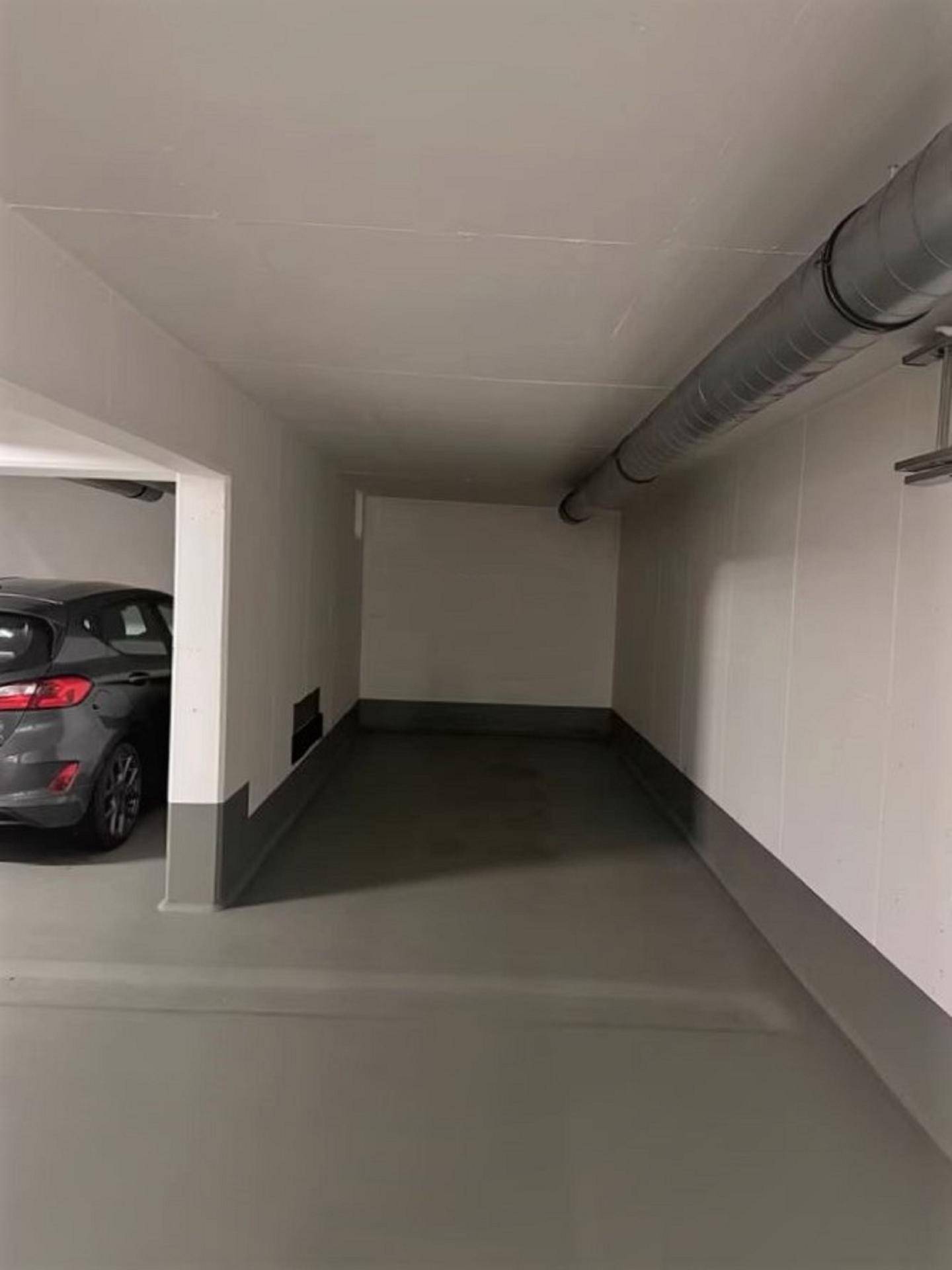 Schmalerer Bereich einer Tiefgarage mit einem geparkten Fahrzeug und sichtbaren Rohren unter der Decke.